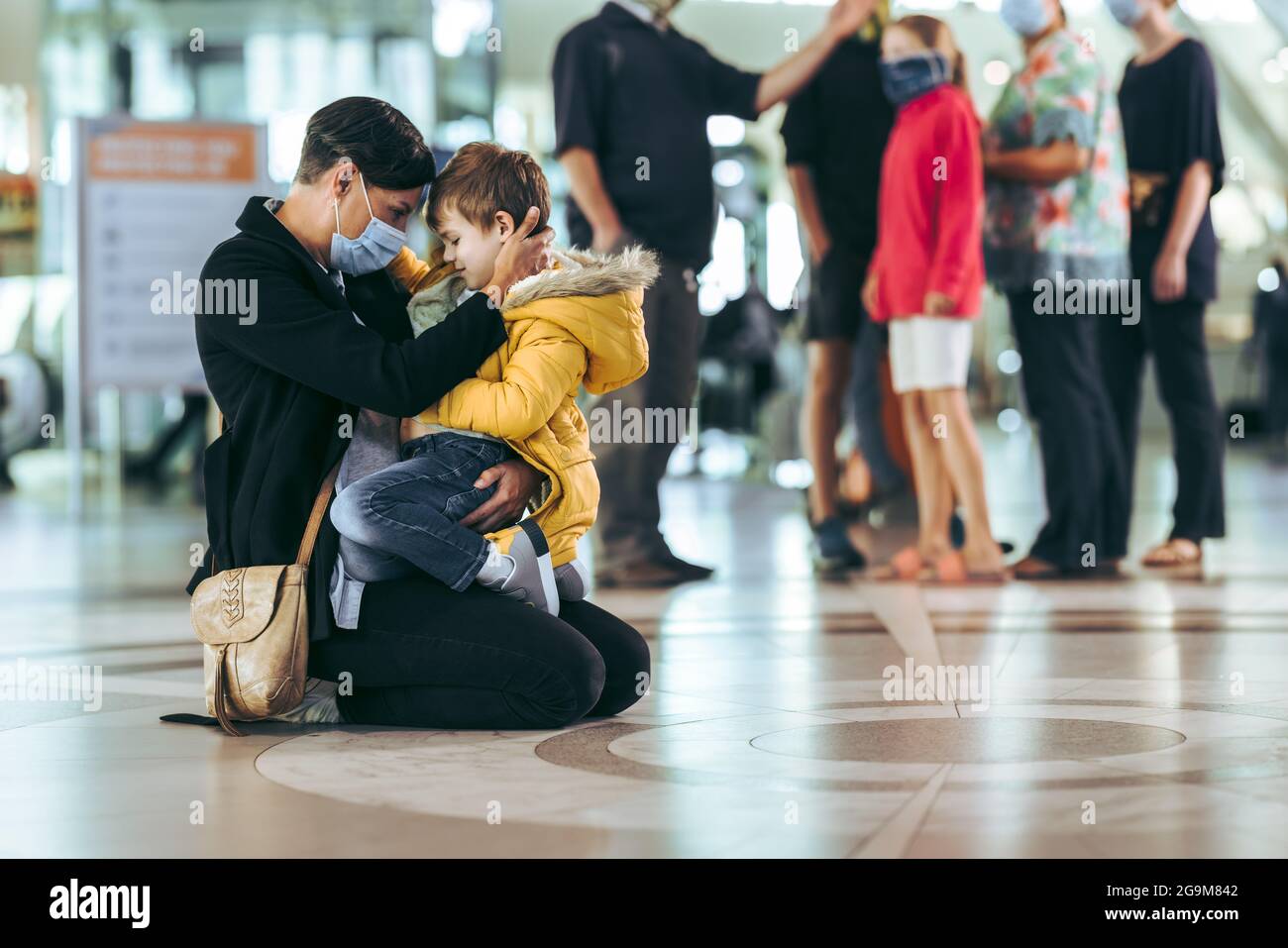 Woman and her boy sitting on floor at airport. Mother in face mask sitting with her son at international airport terminal. Stock Photo