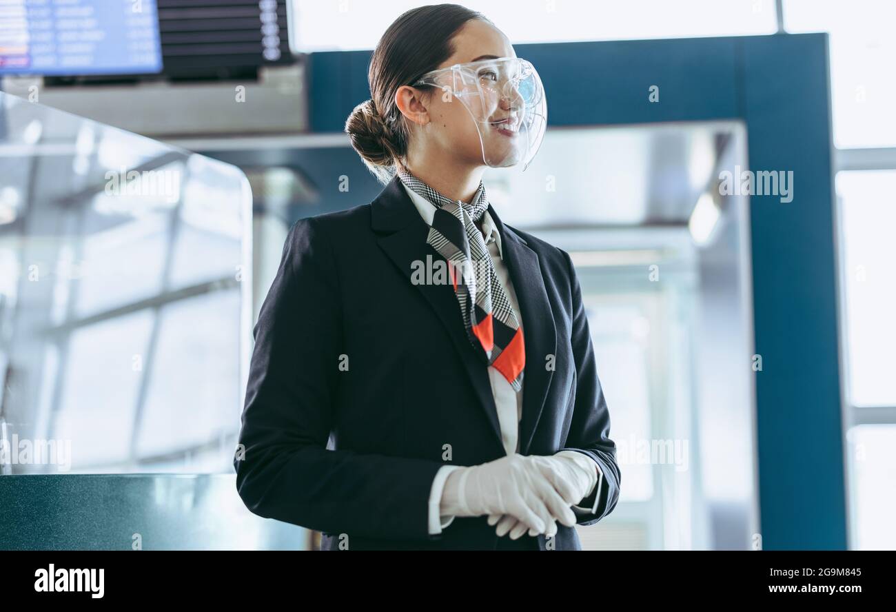 Air hostess in face shield standing at airport. Airport employee at terminal during pandemic