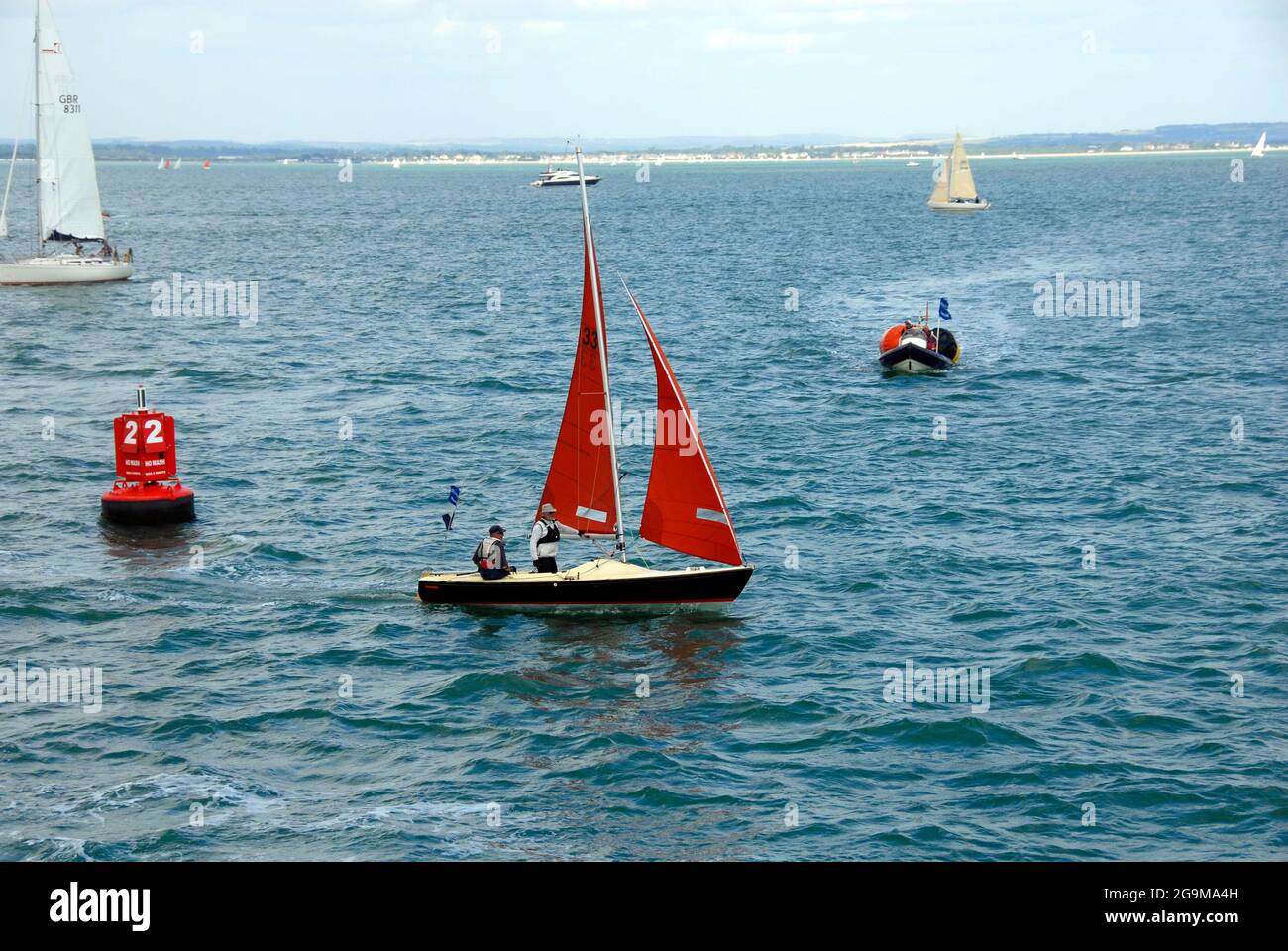 Small yacht with black hull and red/orange sails and two men on board sailing during  Cowes Week regatta, England Stock Photo