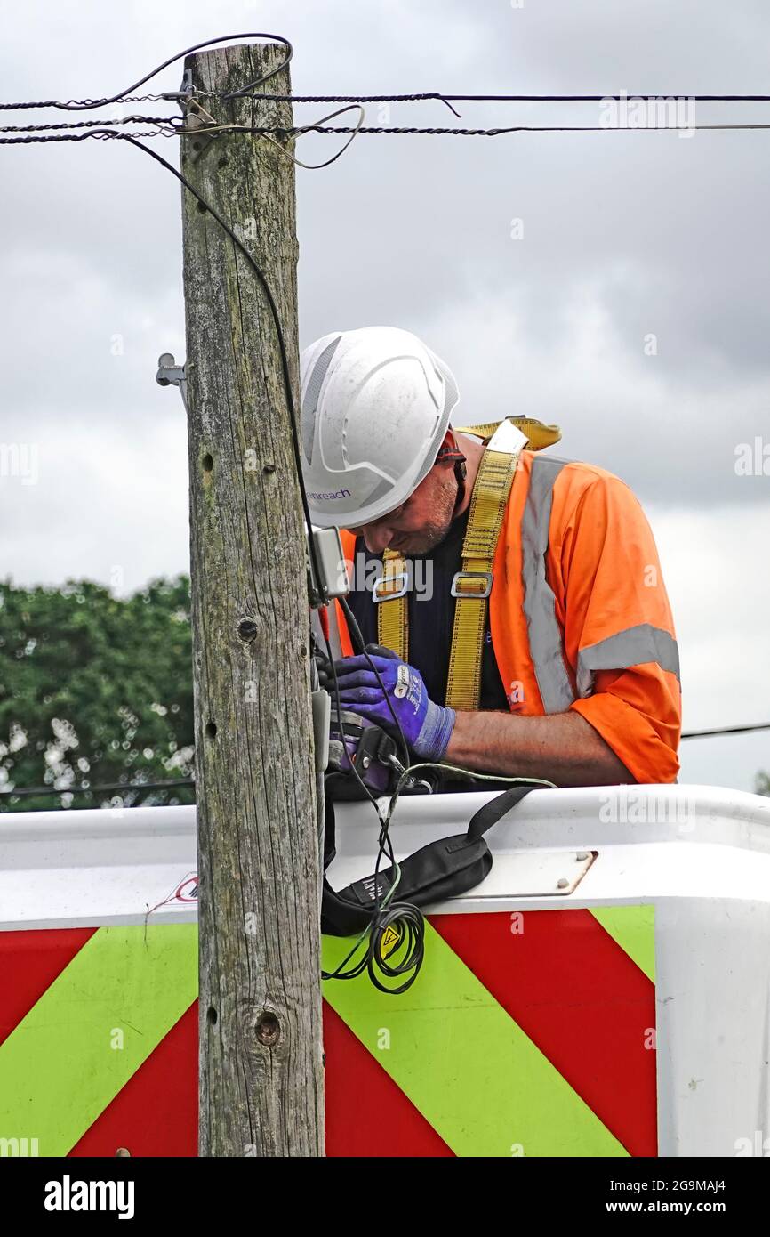 Close up top section timber BT telephone pole & cables Openreach phone engineer working on cherry picker hoist checking fault on domestic line England Stock Photo