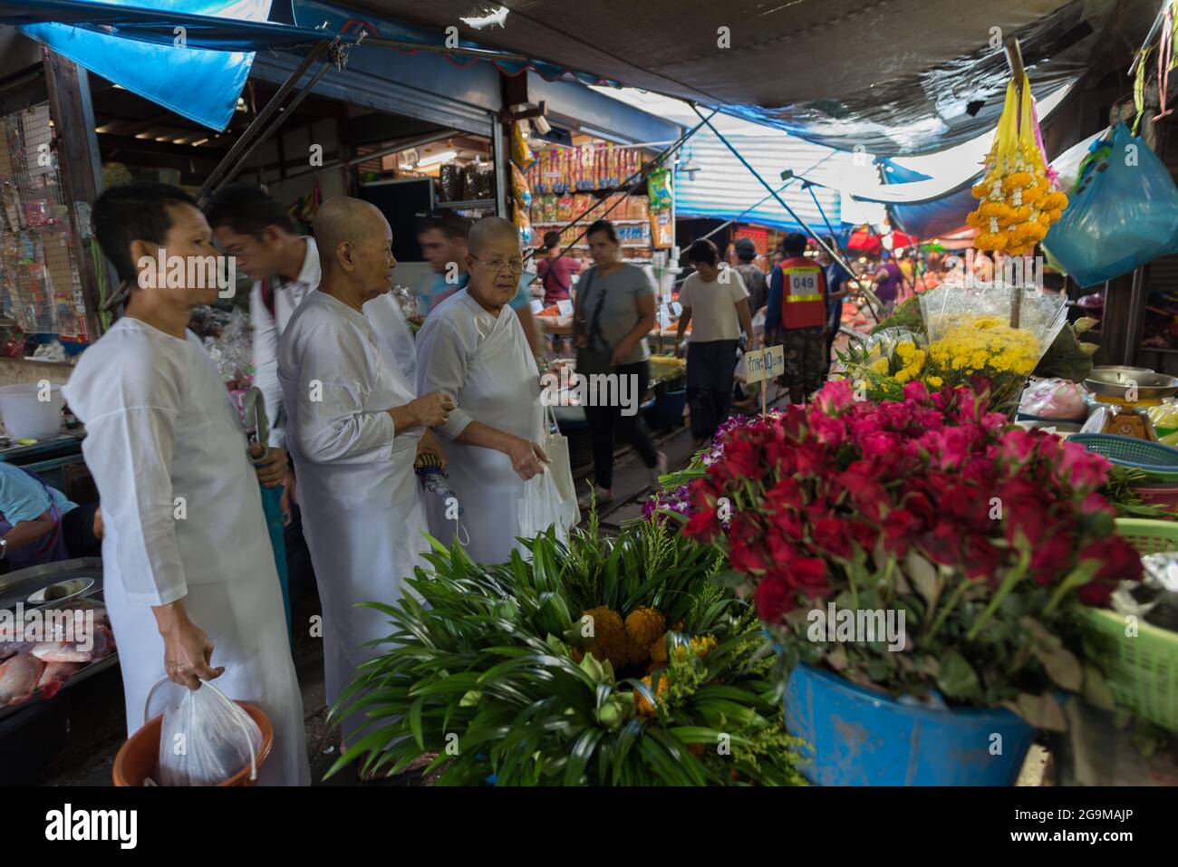 Three Buddhist nuns look to buy flowers in the Maeklong railway market. Stock Photo