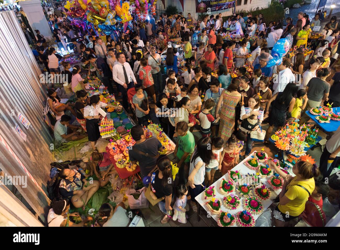 A packed crowd navigates between the stalls of merchants selling krathongs at the exit of Benjasiri park. Stock Photo