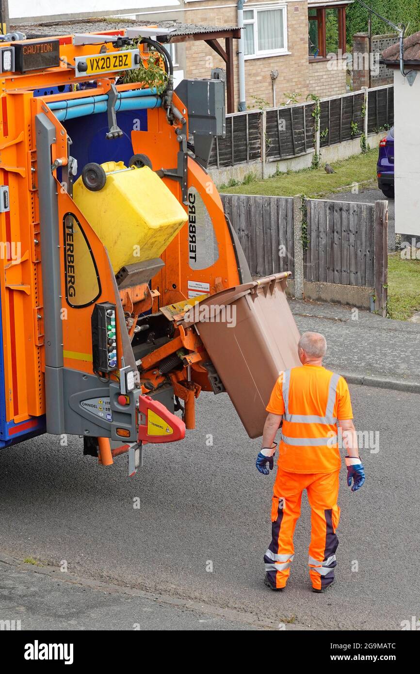 Council dustman worker at back of rubbish bin collection dustcart lorry truck collect green household garden waste in wheelie bin for recycling UK Stock Photo