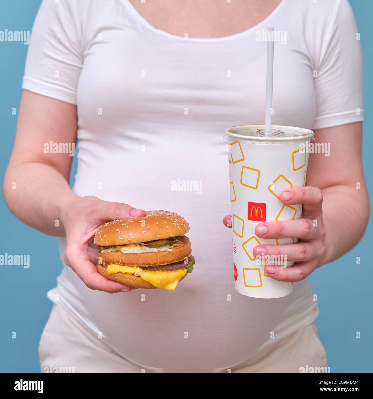 Pregnant woman with a CocaCola and burger from McDonald on a blue