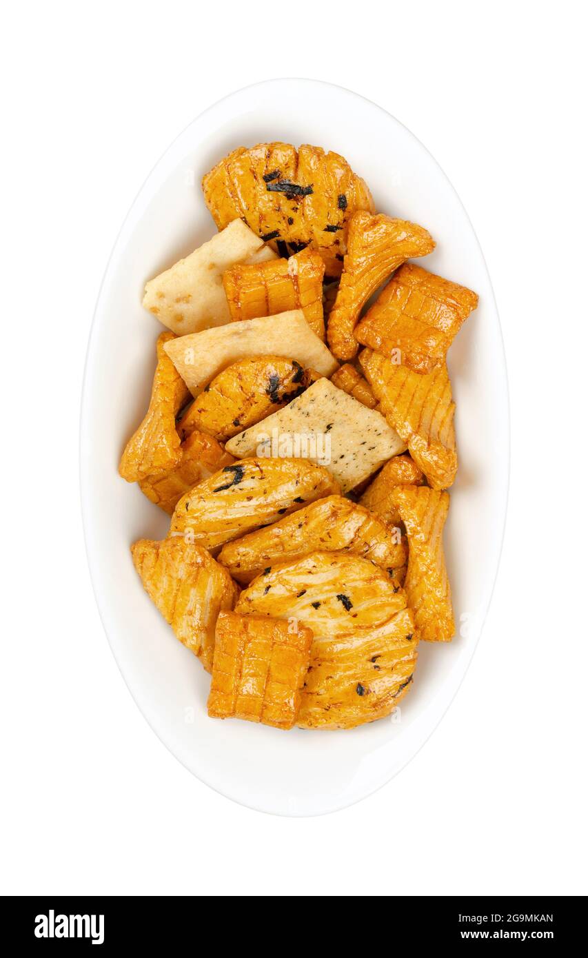 Senbei, Japanese rice crackers, in a white oval bowl. Also sembei, crispy, bite-sized, savory snacks in various shapes and sizes, slightly salted. Stock Photo