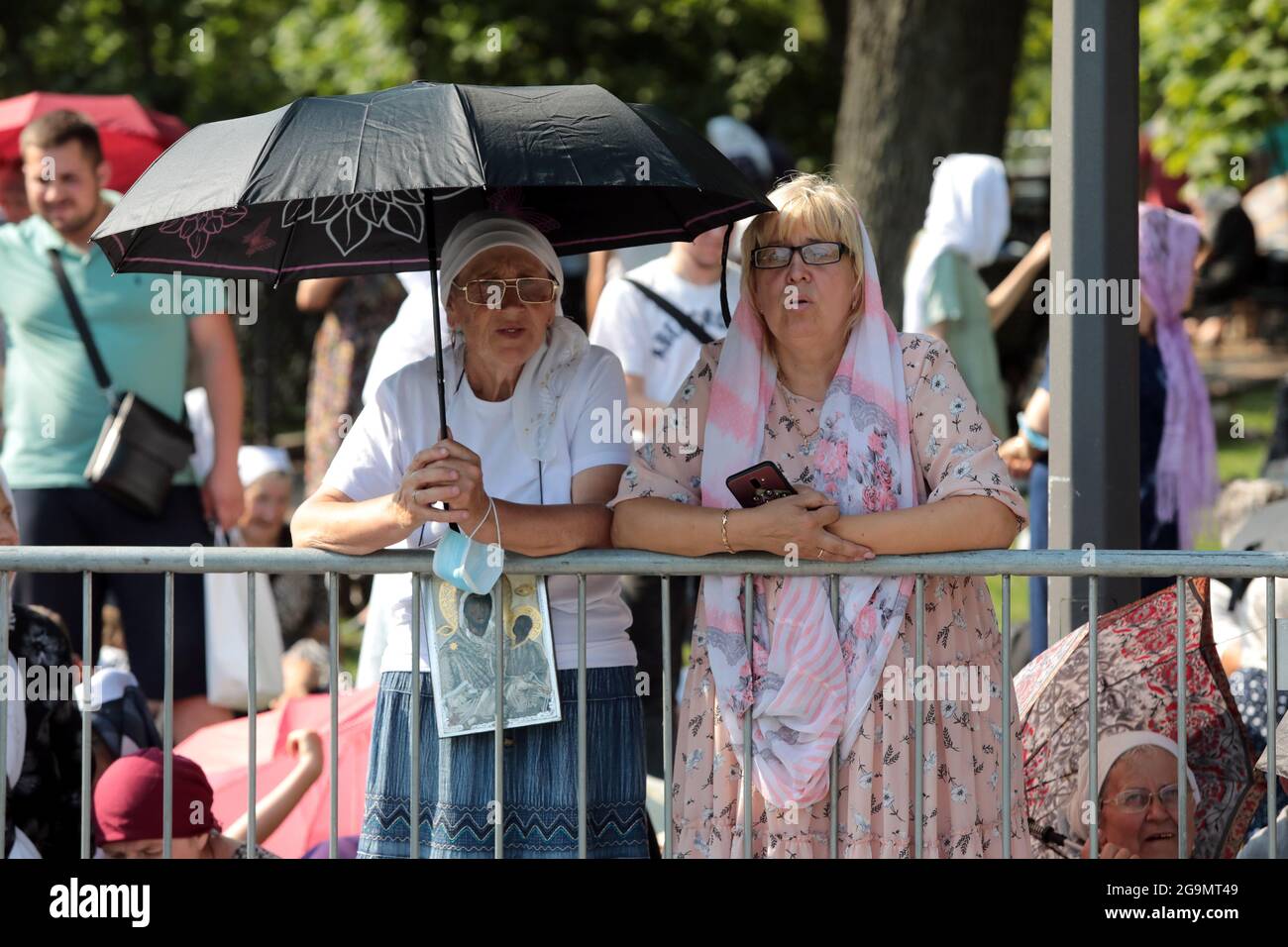 KYIV, UKRAINE - JULY 27, 2021 - Women hide from the sun under an umbrella as they wait for the start of the prayer service on Volodymyrska Hill (St Vo Stock Photo