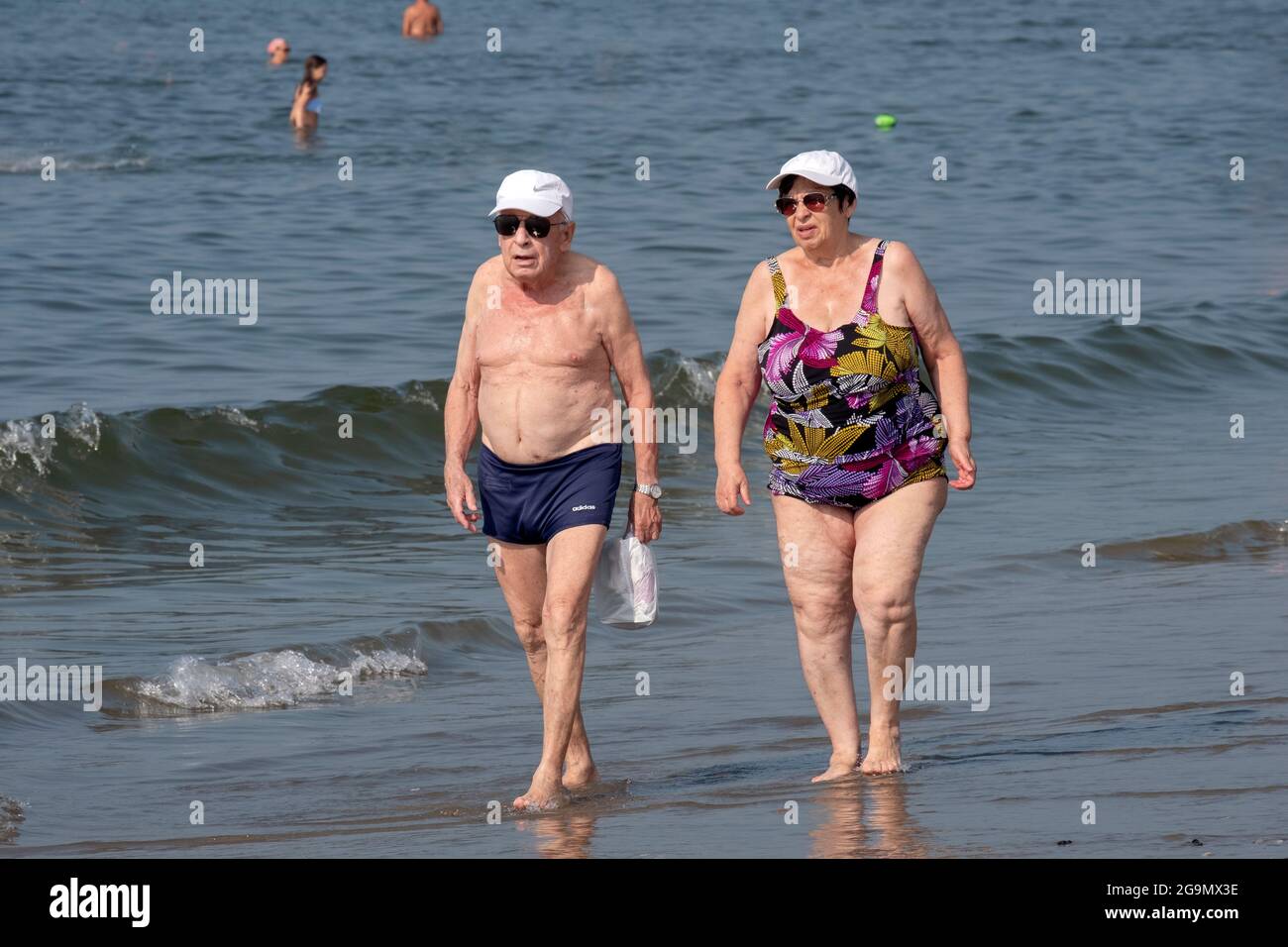 An older couple, presumably husband & wife, walk along the shoreline at Brighton Beach in Brooklyn, New York City. Stock Photo