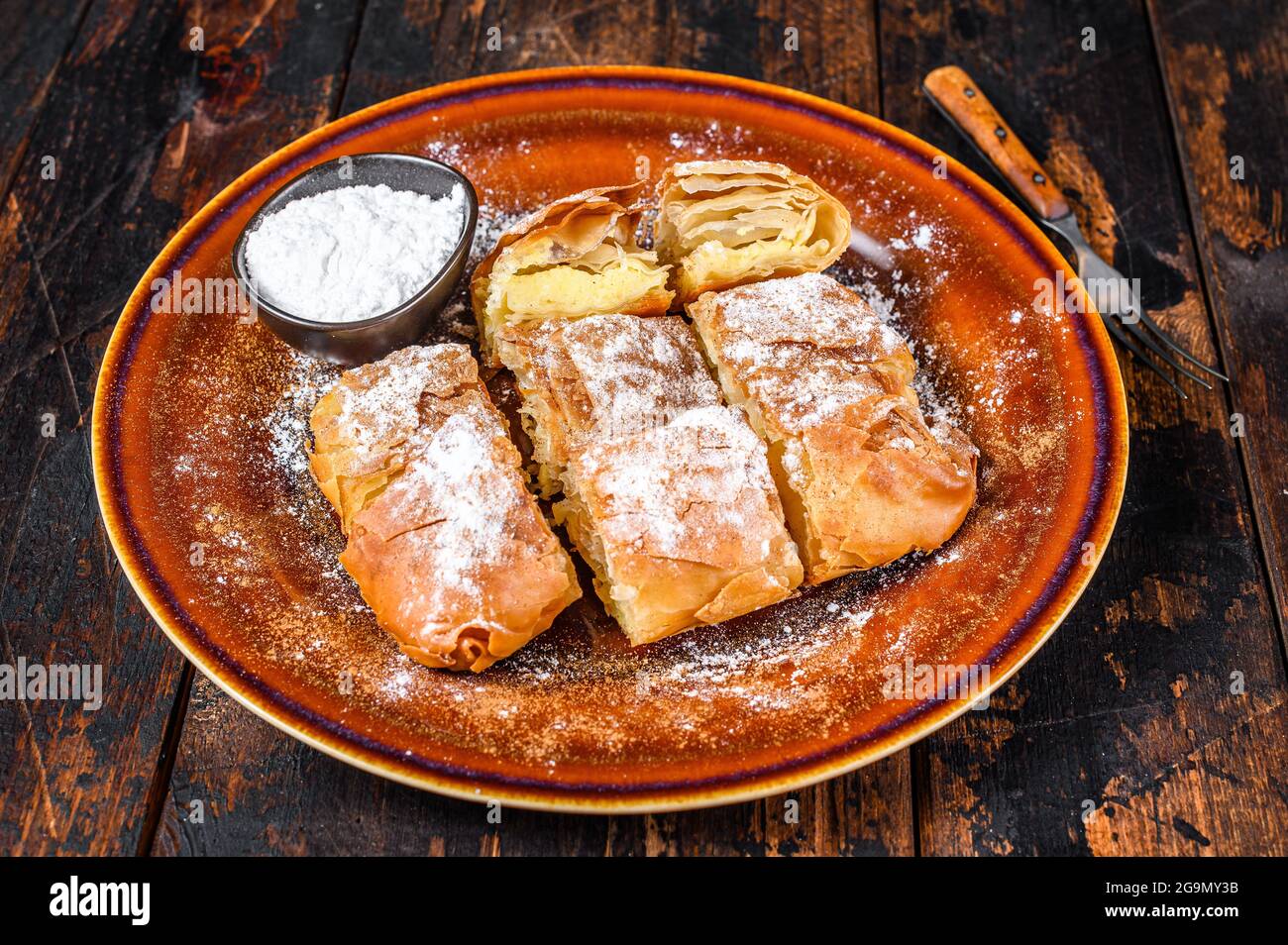 Sliced Greek Bougatsa pie with phyllo dough and semolina custard cream. Dark Wooden background. Top view Stock Photo