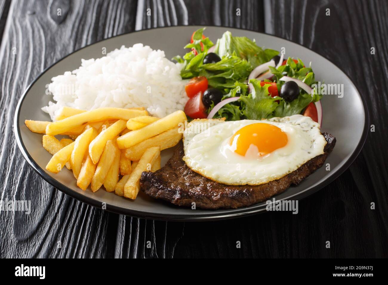 Bitoque is a beloved Portuguese dish that includes lean steak accompanied by rice and french fries topped with a fried egg closeup in the plate on the Stock Photo