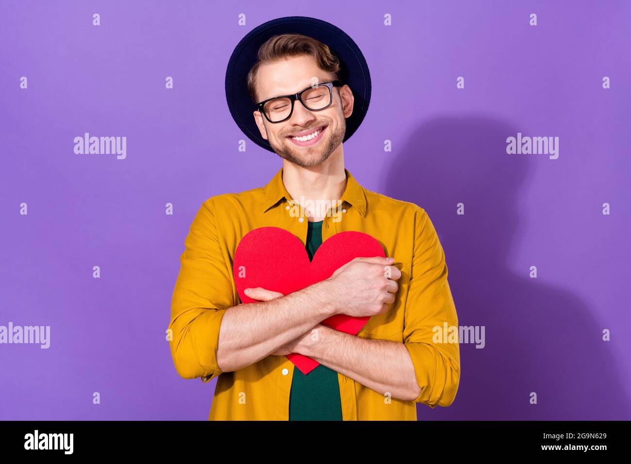Photo of cheerful happy young man adore hold heart shape red paper hug ...