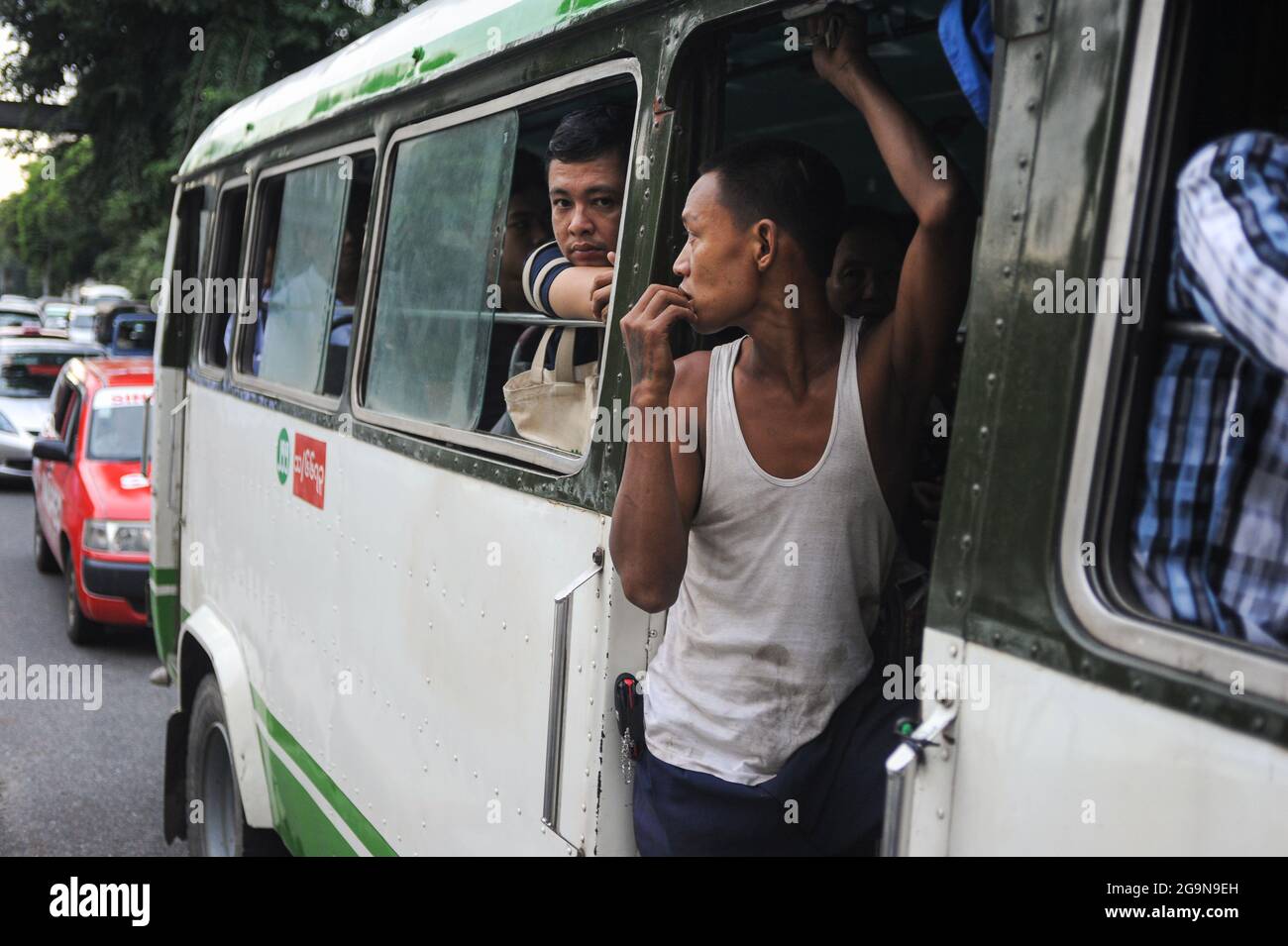 30.09.2013, Yangon, Myanmar, Asia - A bus conductor working in the local transport sector stands in the open door of a crowded bus. Stock Photo