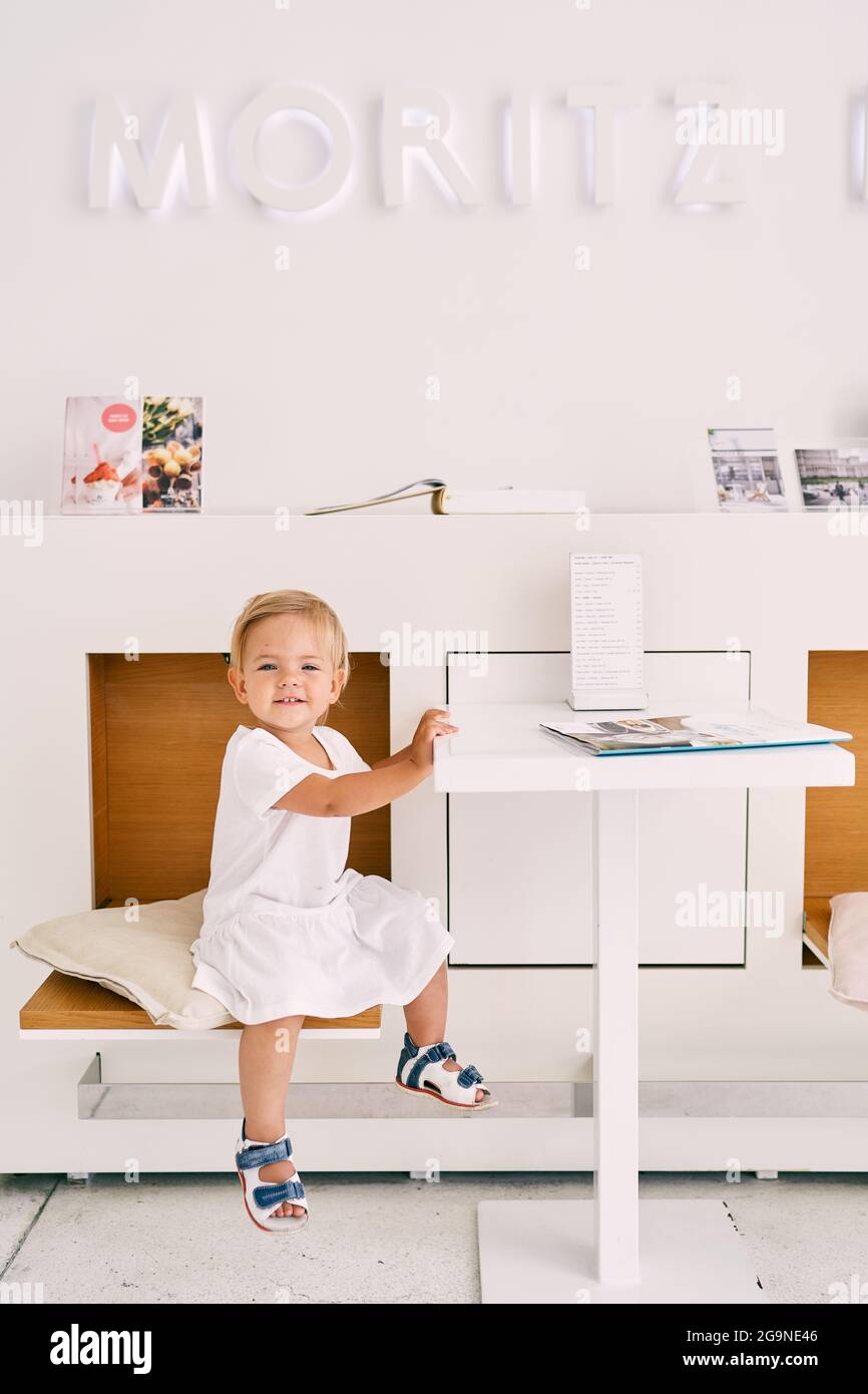 Little smiling girl sits in a cafe at a table on a chair Stock Photo ...