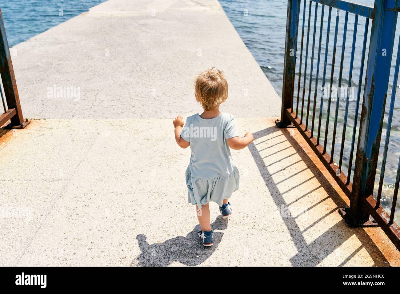 Little girl walks along a concrete pier. Back view Stock Photo - Alamy