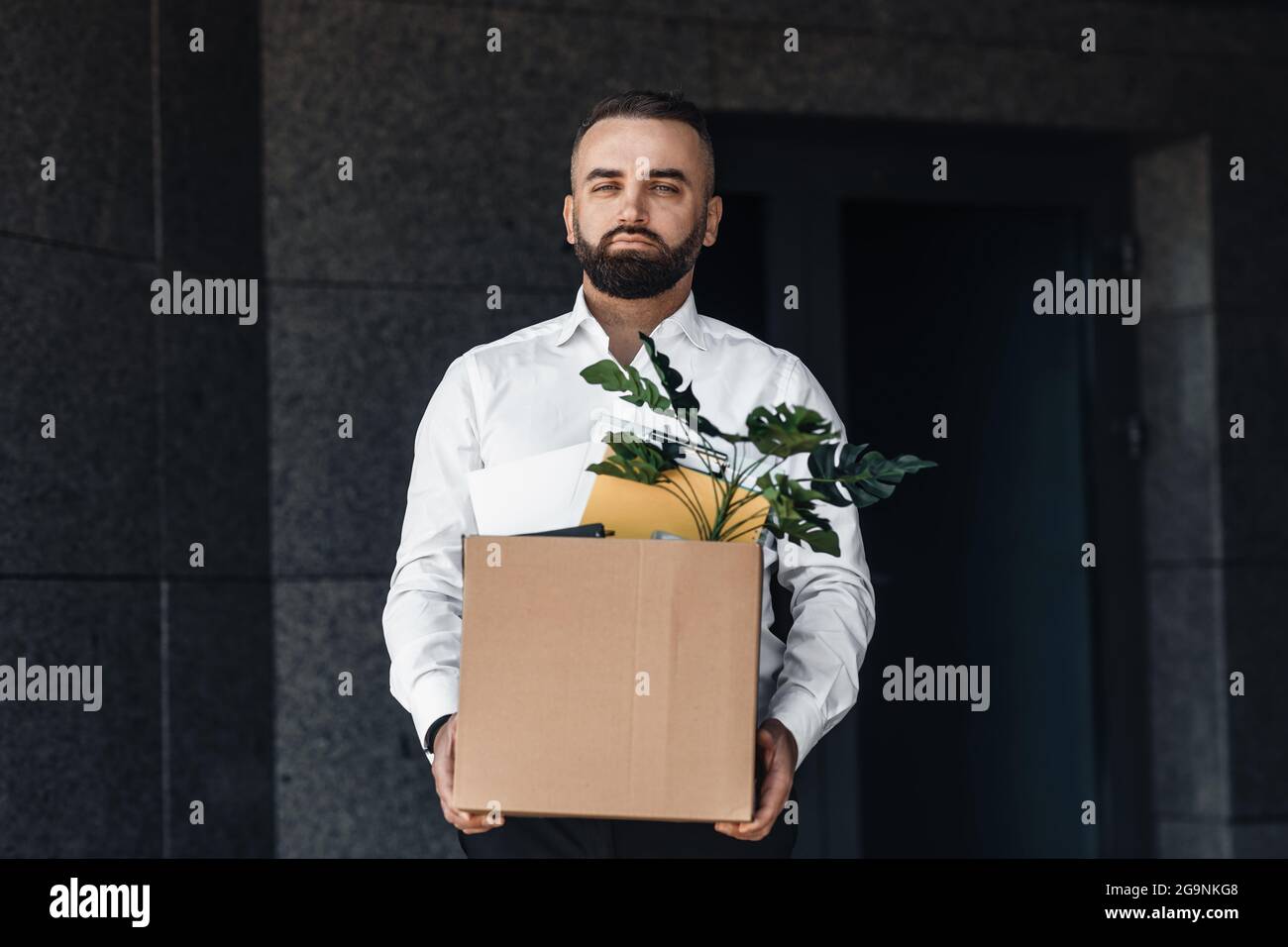 Unemployed man moving out office center with box full of personal stuff, looking sadly to camera Stock Photo