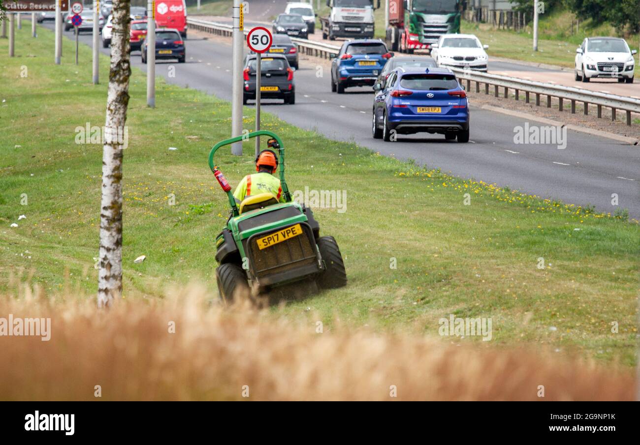 Dundee, Tayside, Scotland, UK. 27th July, 2021. UK Weather: Overcast and humid day across North East Scotland with temperatures reaching 21°C. BEAR Scotland are responsible for managing and maintaining some of the country’s most important roads. Today maintenance workers are busy out mowing the long grass along the Kingsway West dual carriageway in Dundee. Credit: Dundee Photographics/Alamy Live News Stock Photo