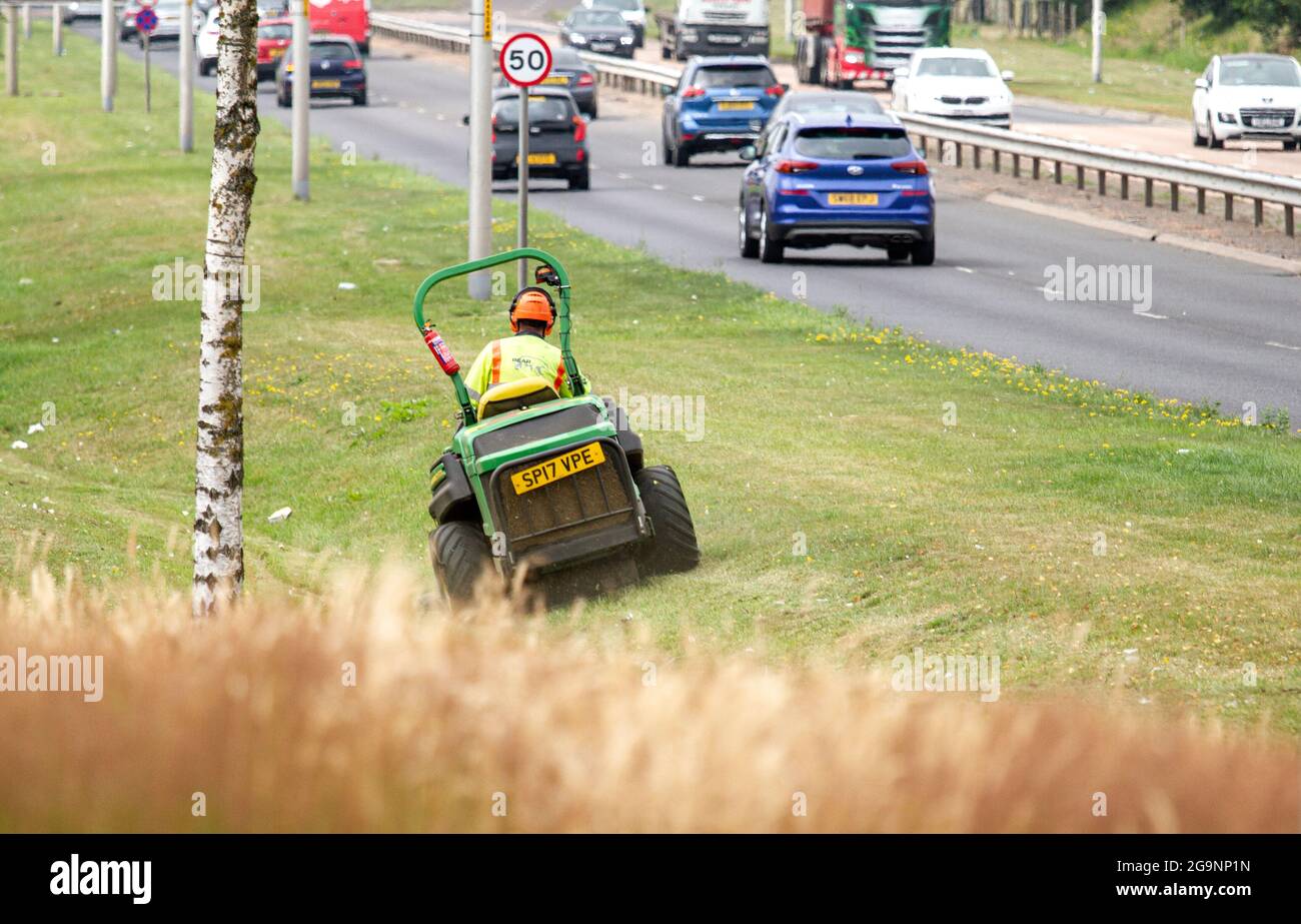 Dundee, Tayside, Scotland, UK. 27th July, 2021. UK Weather: Overcast and humid day across North East Scotland with temperatures reaching 21°C. BEAR Scotland are responsible for managing and maintaining some of the country’s most important roads. Today maintenance workers are busy out mowing the long grass along the Kingsway West dual carriageway in Dundee. Credit: Dundee Photographics/Alamy Live News Stock Photo