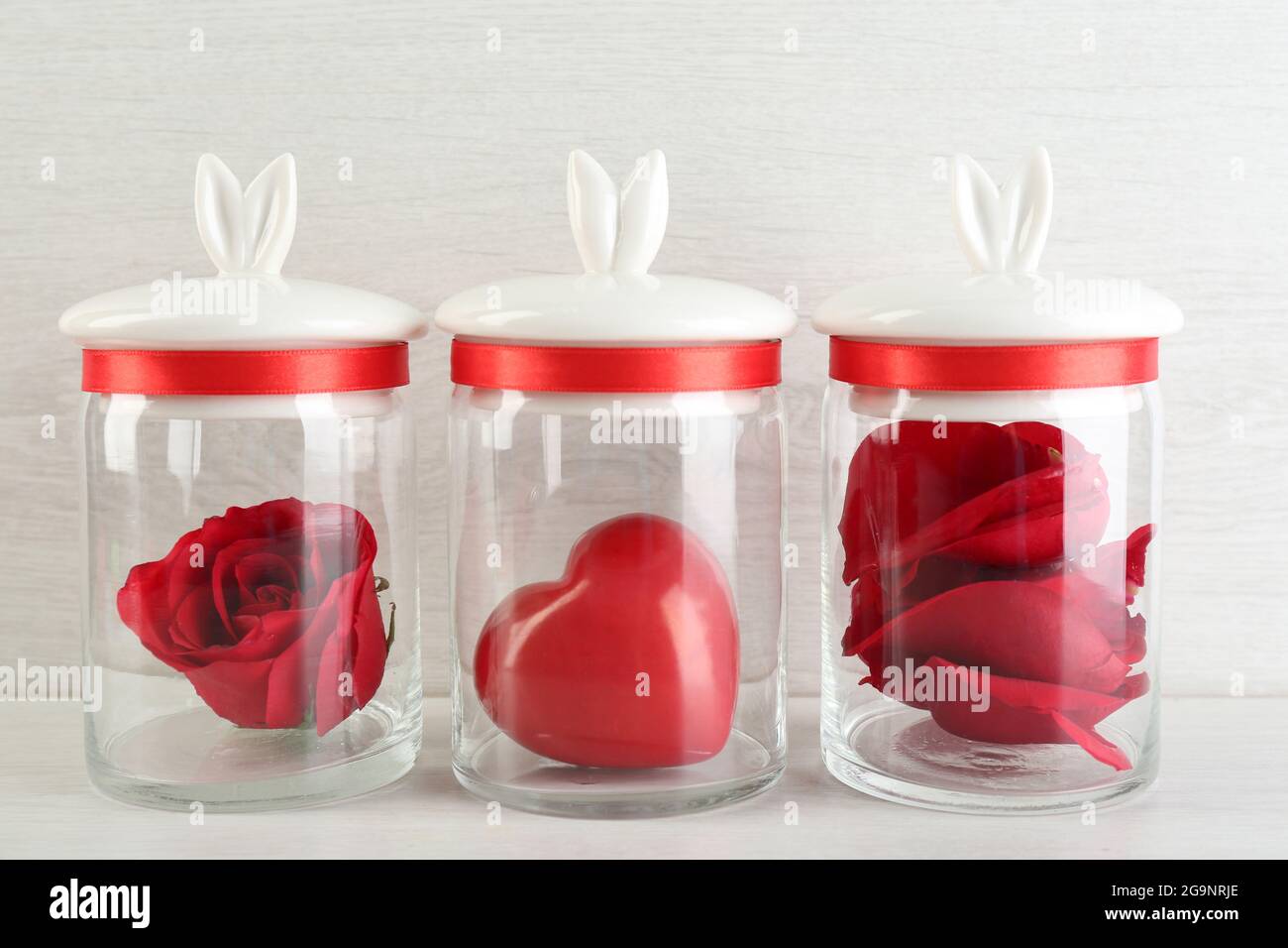 Rose flower, petals and decorative heart in glass jars on light