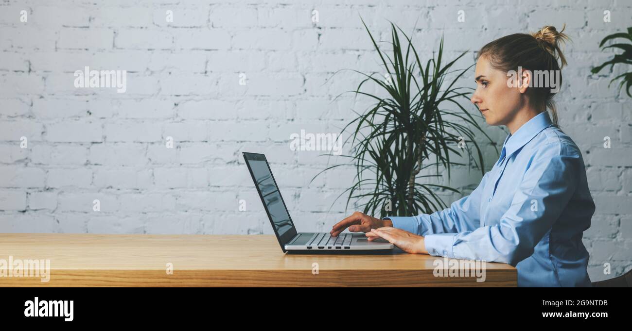 business woman working on laptop in modern office against white brick wall background. banner copy space Stock Photo