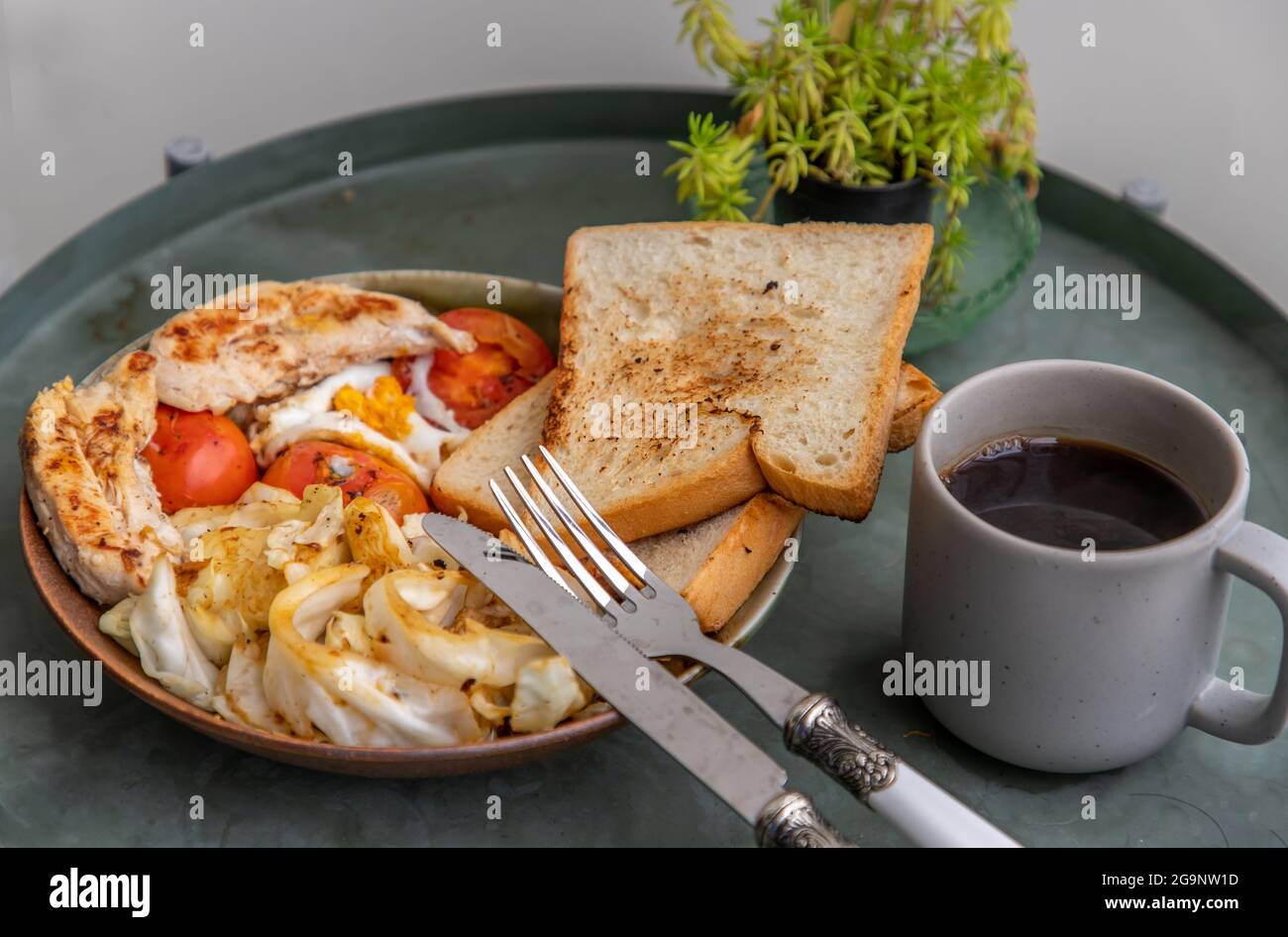 Breakfast with Baked chicken, Fried egg, tomato, toast bread and Fried cabbage on ceramic plate serve with black coffee. Selective focuse. Stock Photo