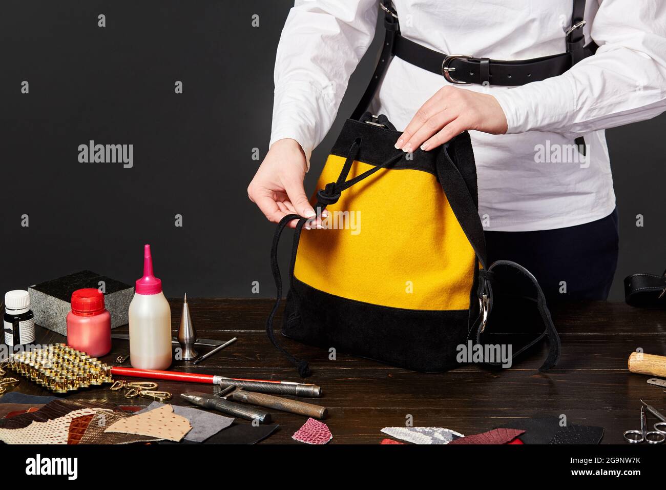 Female leathercrafter tightening strap of black and yellow suede bag at