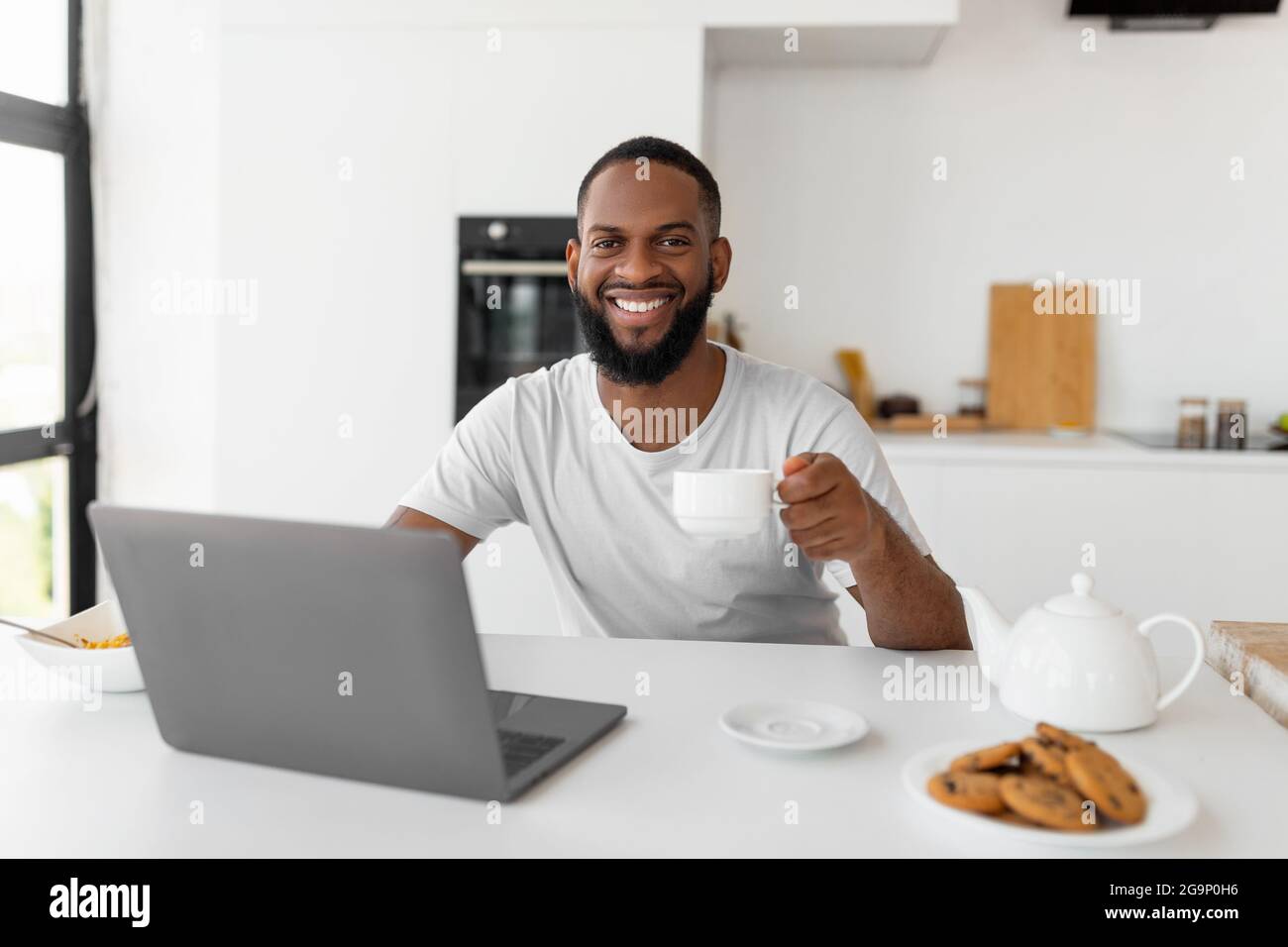 African American man using laptop drinking coffee looking at camera Stock Photo