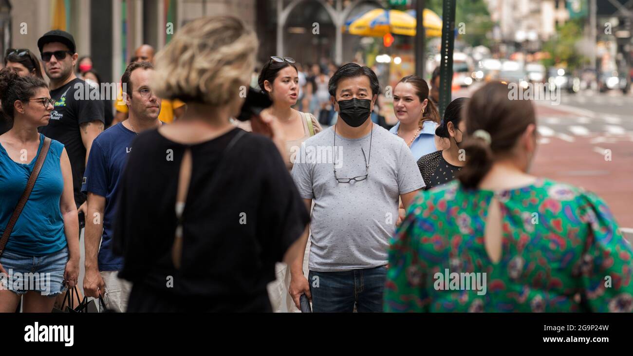 Sunday afternoon on 5th Avenue in New York City, 25/07/21.  After New York’s crowded streets fell quiet during the COVID-19 pandemic, people are out on the streets again, many are out without wearing a mask or face covering. Photo shows man (Right) wearing a face covering while others waiting to cross 51st street on 5th Avenue do not. Stock Photo