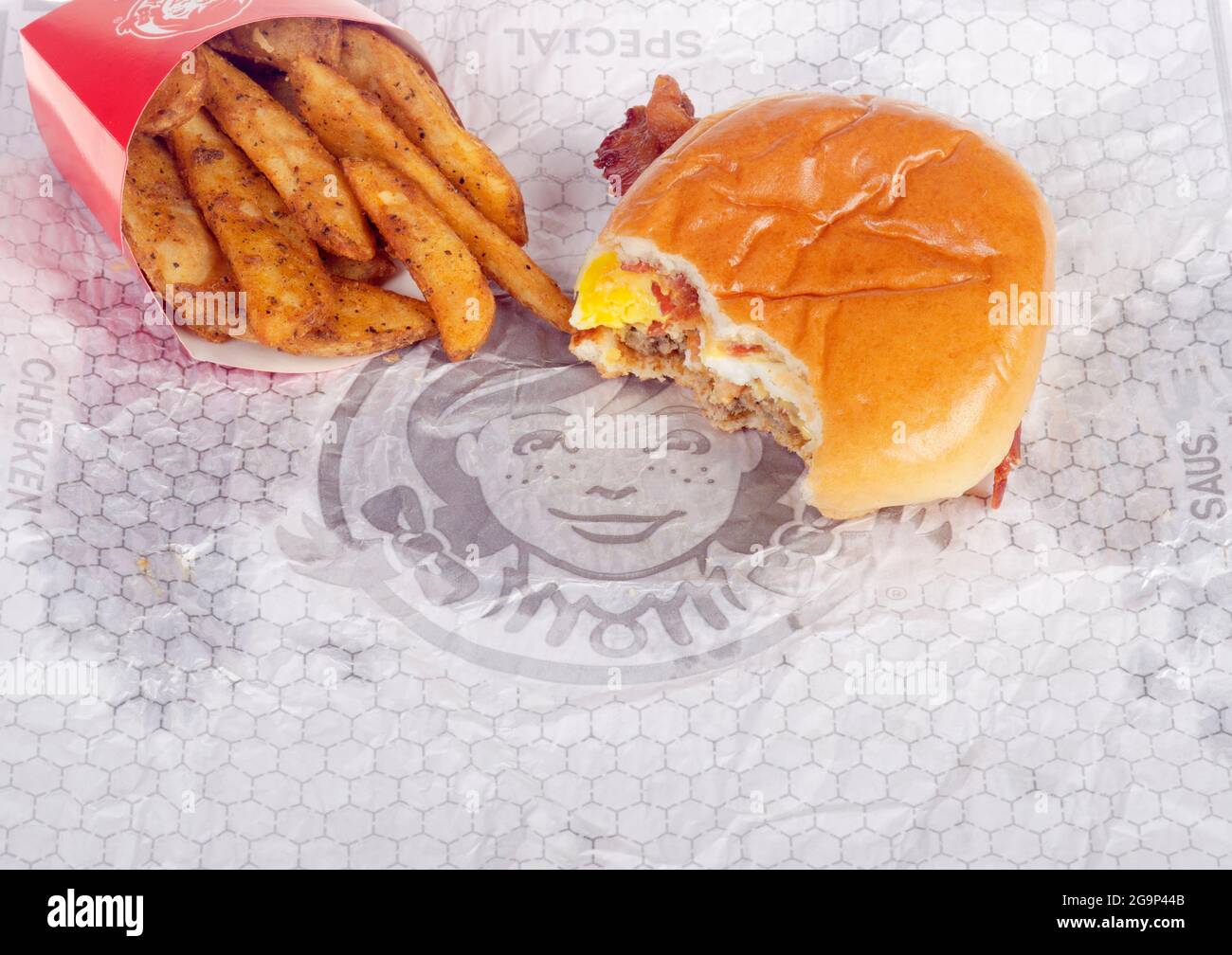 Wendy's baconator  breakfast Sandwich on wrapper with bite taken and seasoned potatoes with bacon, egg, sausage and cheese Stock Photo