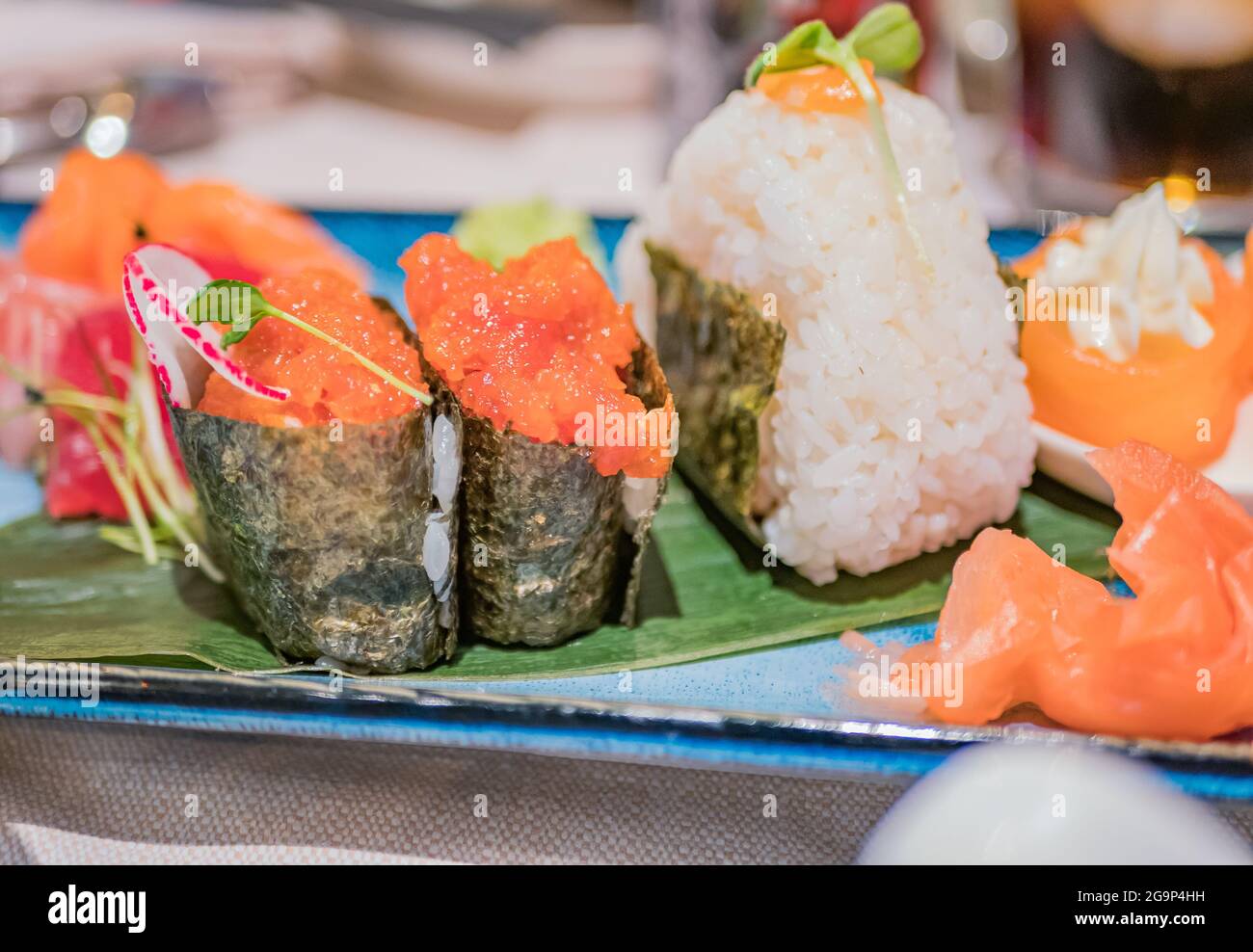 Typical Japanese dish of raw salmon with rice wrapped with dried seaweed and vegetables on a blue plate Stock Photo