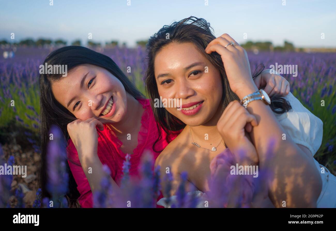young happy and beautiful Asian korean woman playing on lavender flowers field with her hispanic girlfriend enjoying sweet holidays together relaxed a Stock Photo