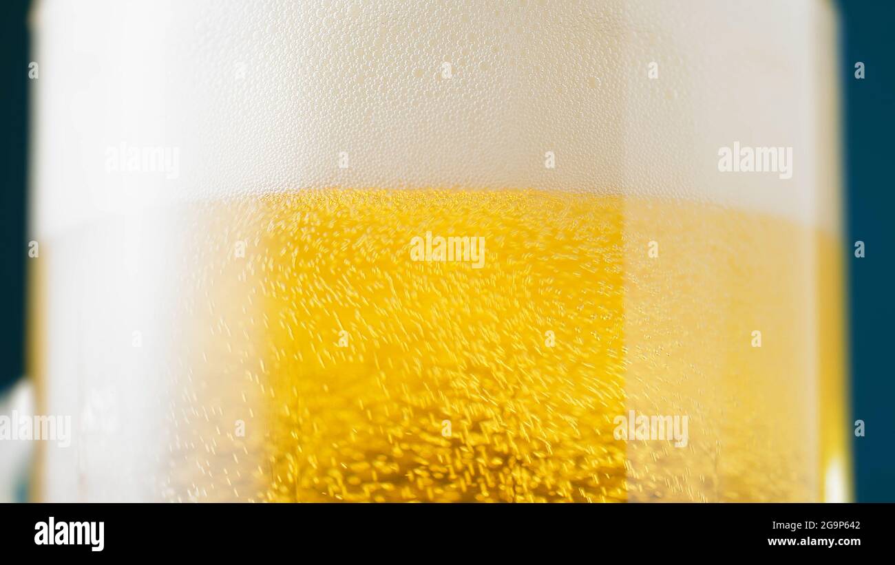 Pouring beer into glass from bottle. Half pint of frothy fresh lager beer on table. Side view Stock Photo