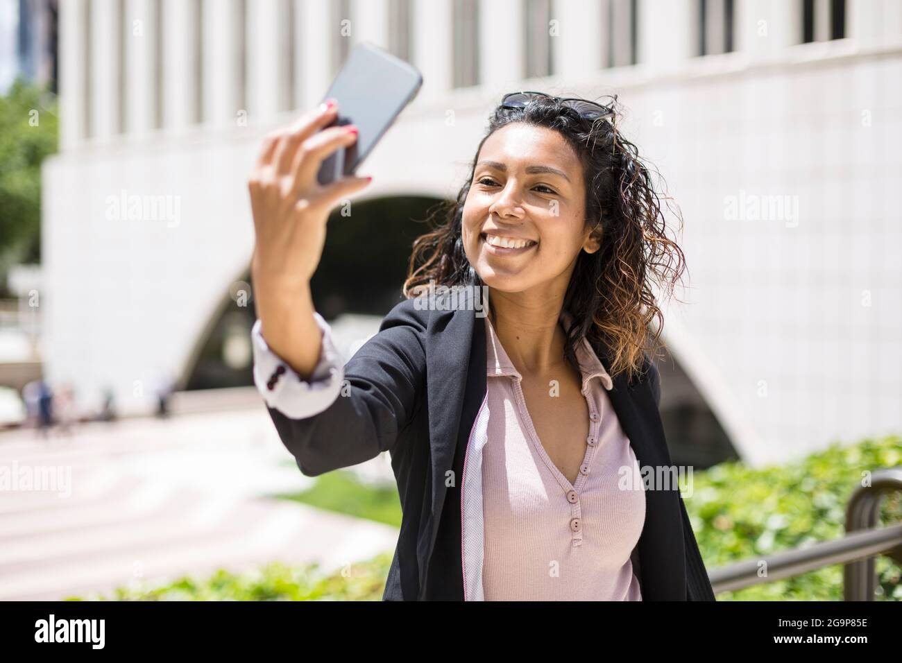 Young smiling hispanic american woman taking a selfie outdoors with her smart phone. Space for text. Stock Photo