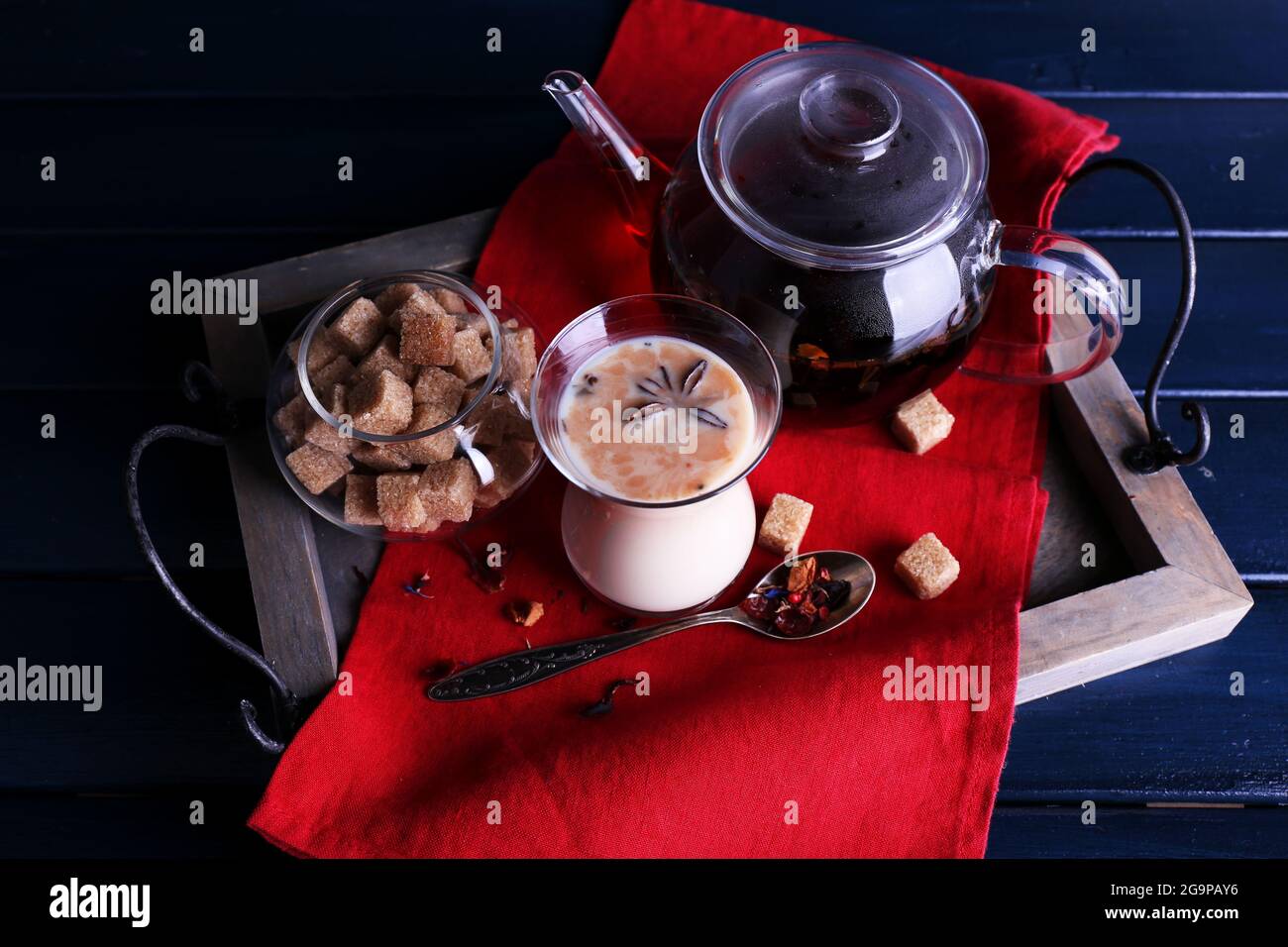 Black tea with milk and lump sugar on wooden tray with napkin and color