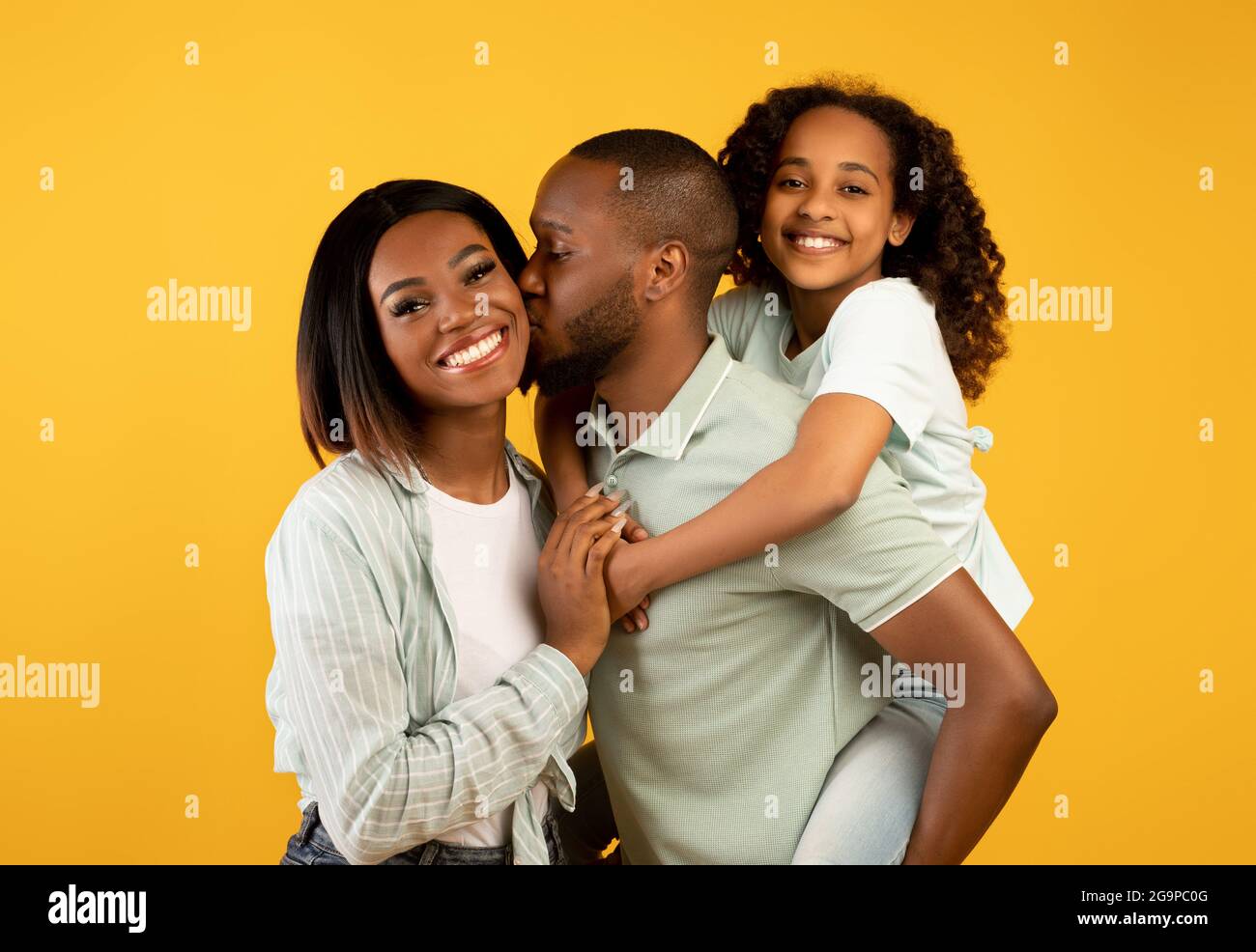 Happy african american family of three with adorable daughter, posing and smiling to camera over yellow background Stock Photo