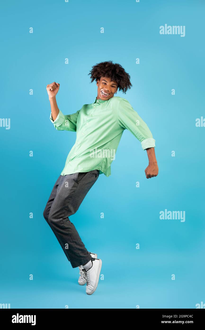 Joyful african american teenage guy standing on tiptoes, fooling and having fun over blue background Stock Photo