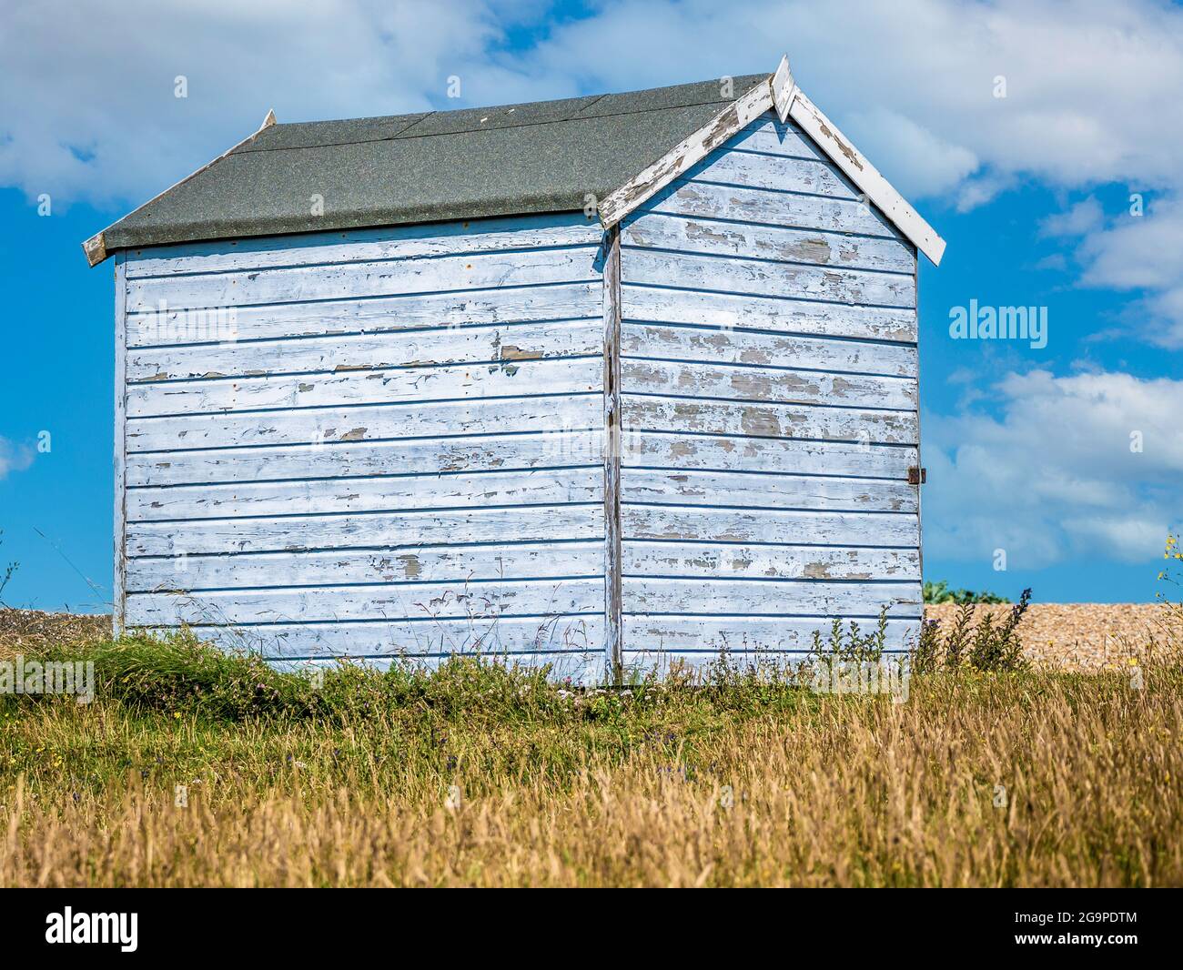 Landscape of a pale blue wooden weathered beach hut with flaking paint by the sea, taken in Greatstone New Romney Kent England on the 17th July 2021 Stock Photo