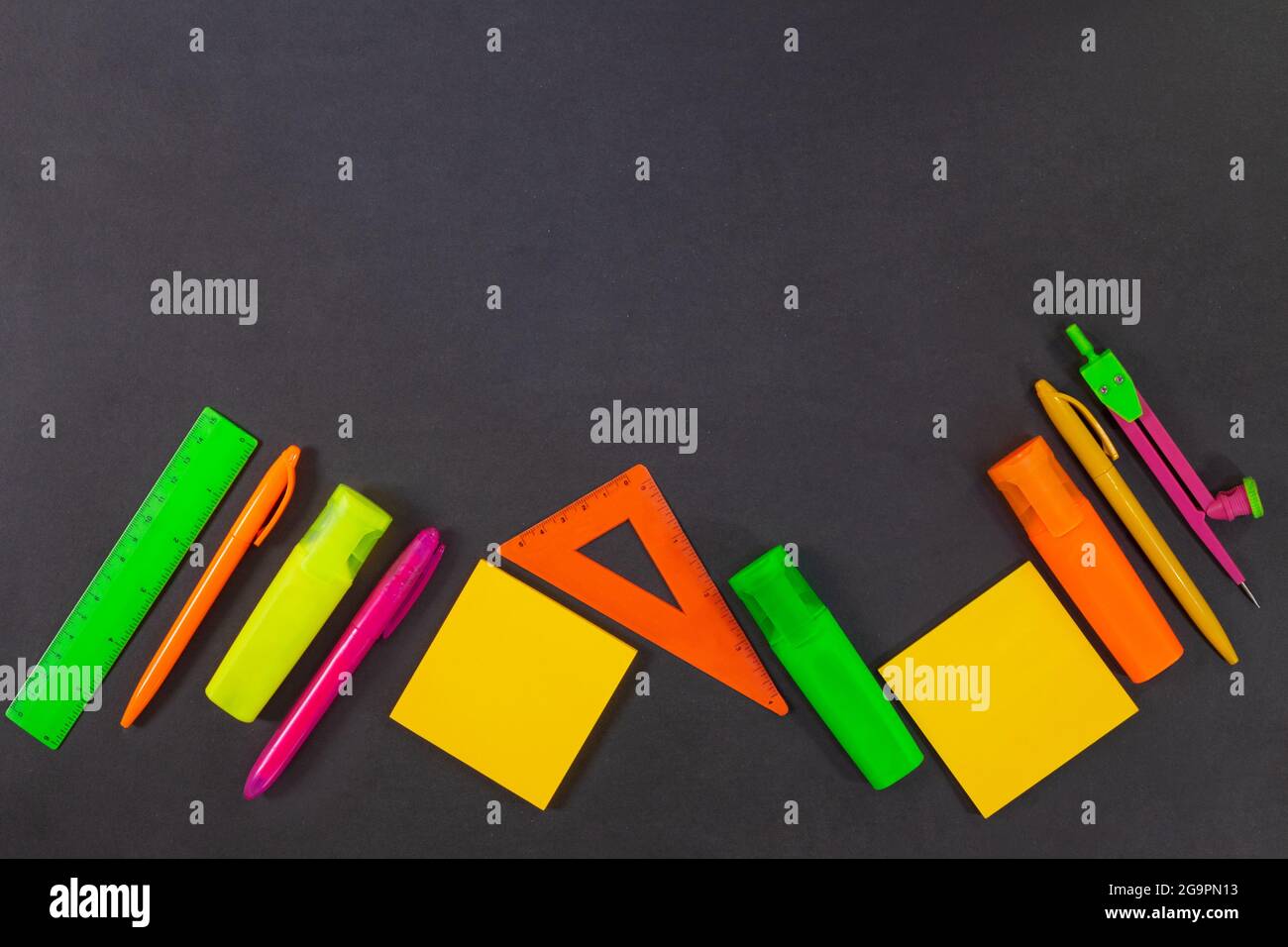 Back to school. Green, yellow, pink, orange office supplies are on the black board, the table. Top view. Rulers, markers, felt tip pens, compasses, pe Stock Photo