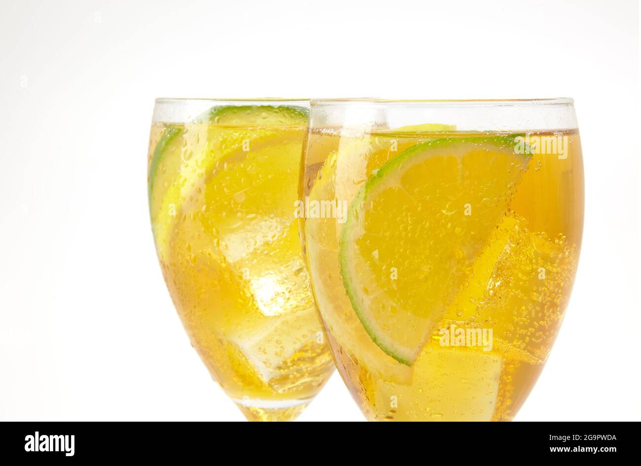 Two stemmed glasses with ice tea and lemon and lime slices on white Stock Photo