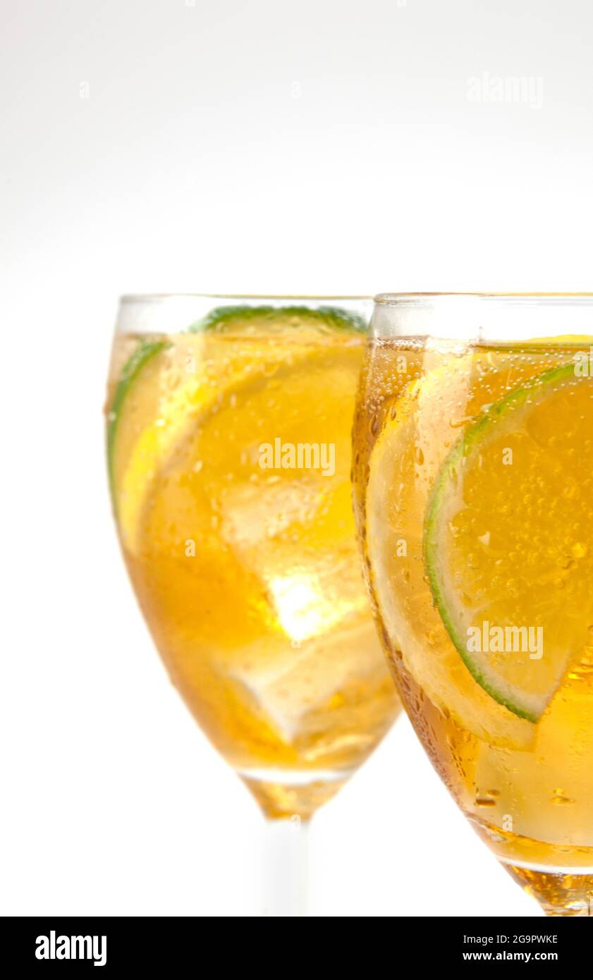 Two stemmed glasses with ice tea and lemon and lime slices on white Stock Photo