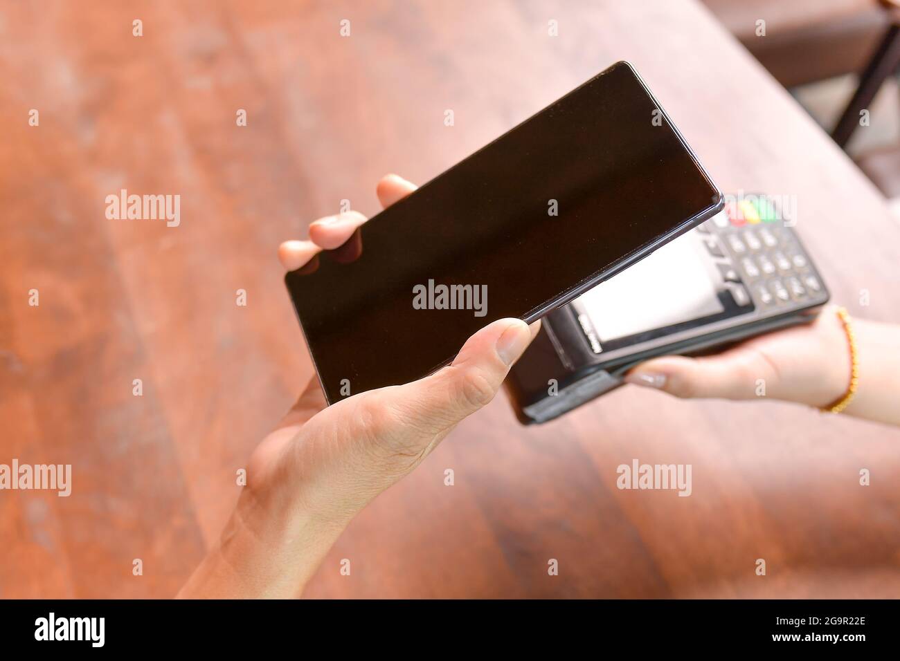 Closeup of a customer using her smartphone and nfs technology to payment Stock Photo