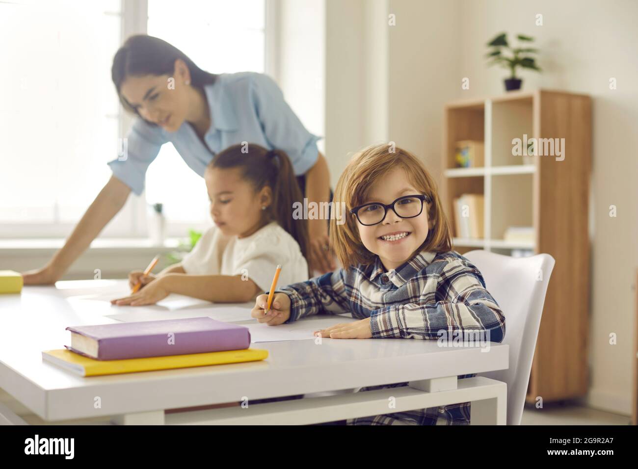 Portrait of cute little elementary student in glasses sitting at his ...