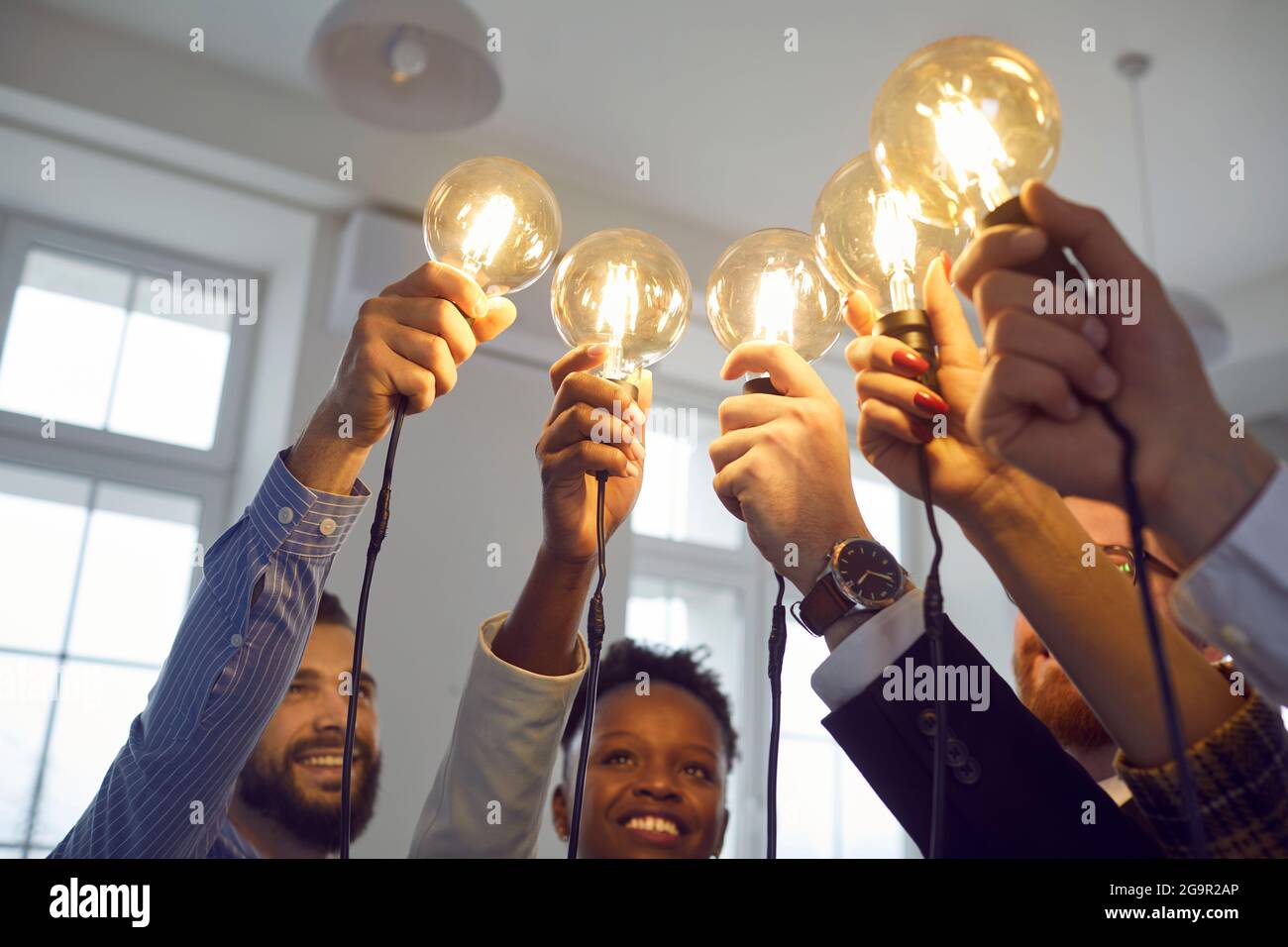 Interracial group of people standing together with raised lightbulb office shot Stock Photo