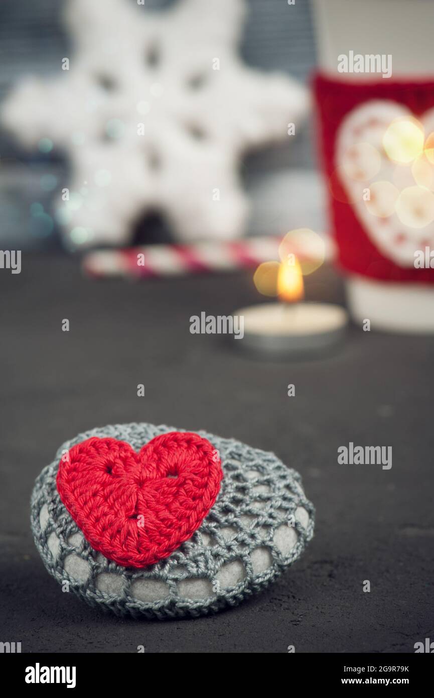 Christmas decoration crochet stone with red heart. Mug and warmer over rustic wooden background Stock Photo