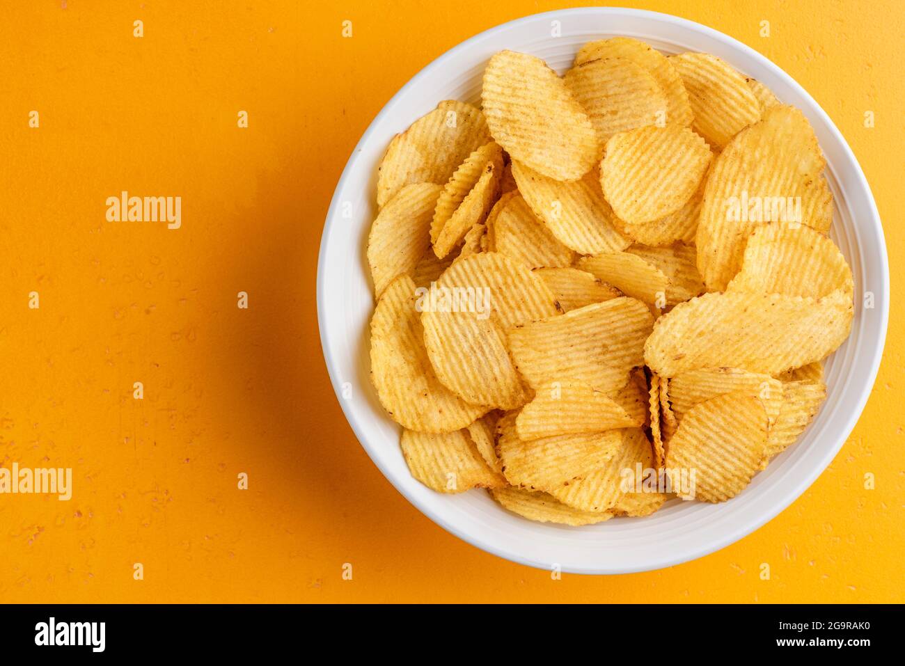 Potato chips in bowl on yellow background, top view. Unhealthy food