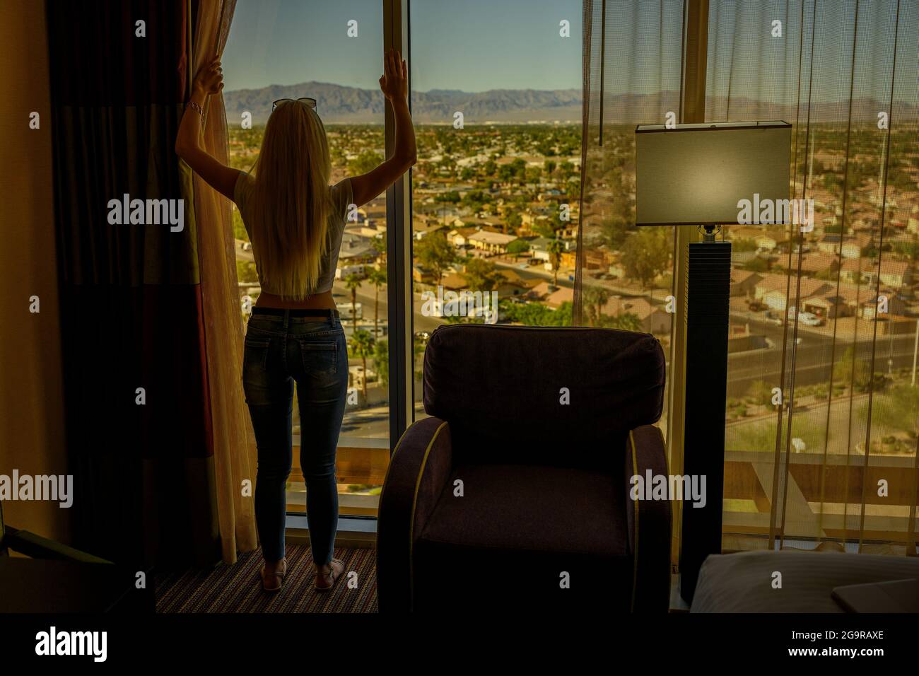 Full length silhouette of a young blonde woman in her luxury apartment in a highrise building looking through her window and watching the city laying Stock Photo