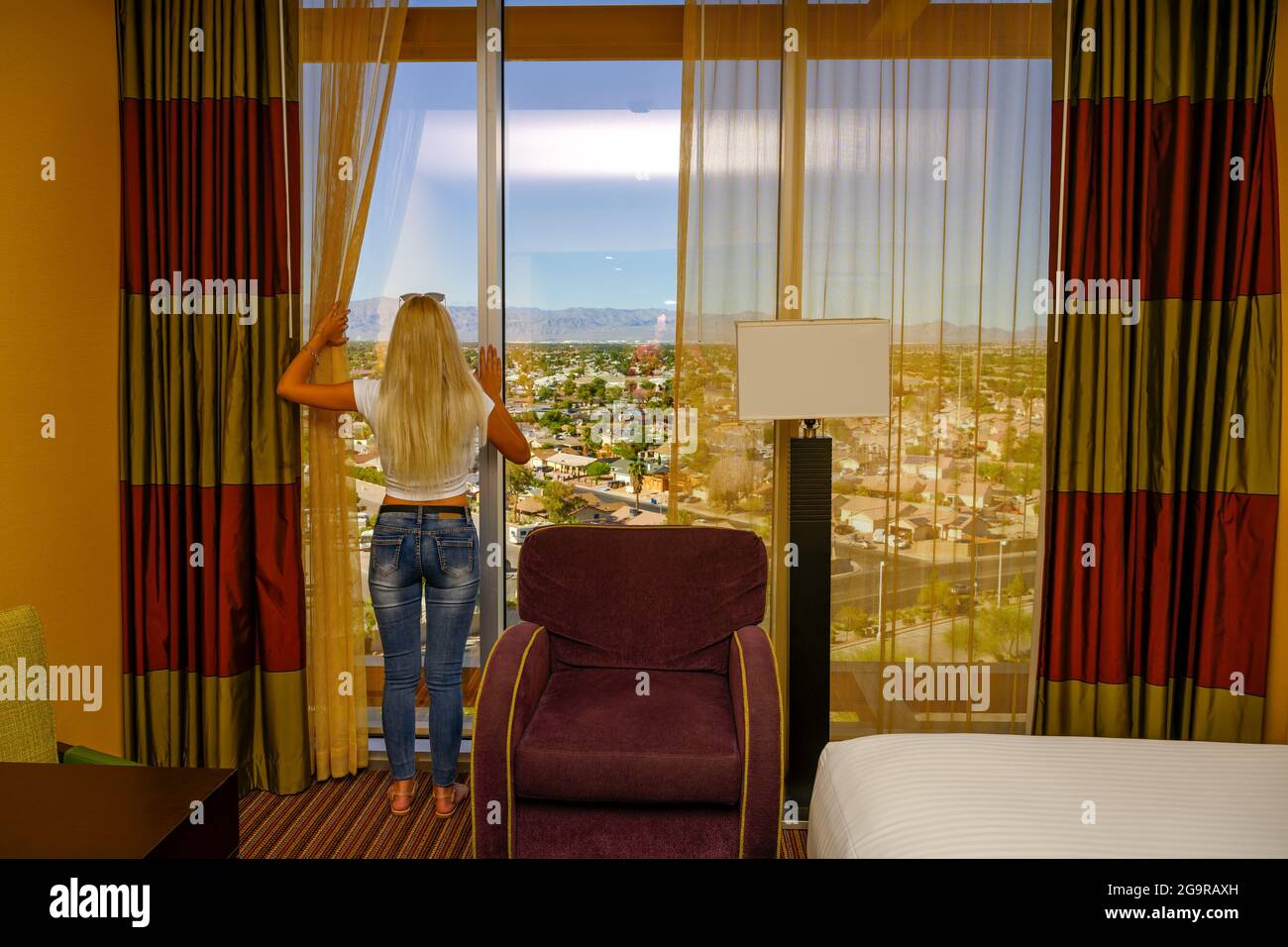Full length photo of a young blonde woman in her luxury apartment in a highrise building looking through her window and watching the city laying down Stock Photo