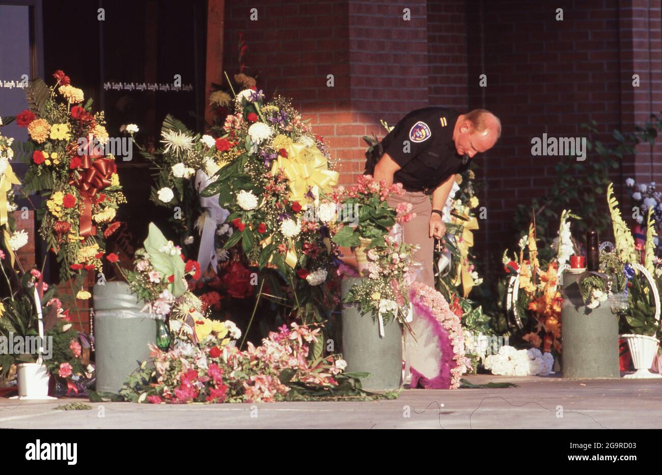 Killeen Texas USA, October 1991: Policeman looks at flowers left in memory of the victims of a mass shooting at Luby's Cafeteria in Killeen. on October 16. George Hennard, a 35-year-old Killeen resident, crashed a pickup into the eatery and shot 23 lunch-time diners and staff to death before killing himself. ©Bob Daemmrich Stock Photo