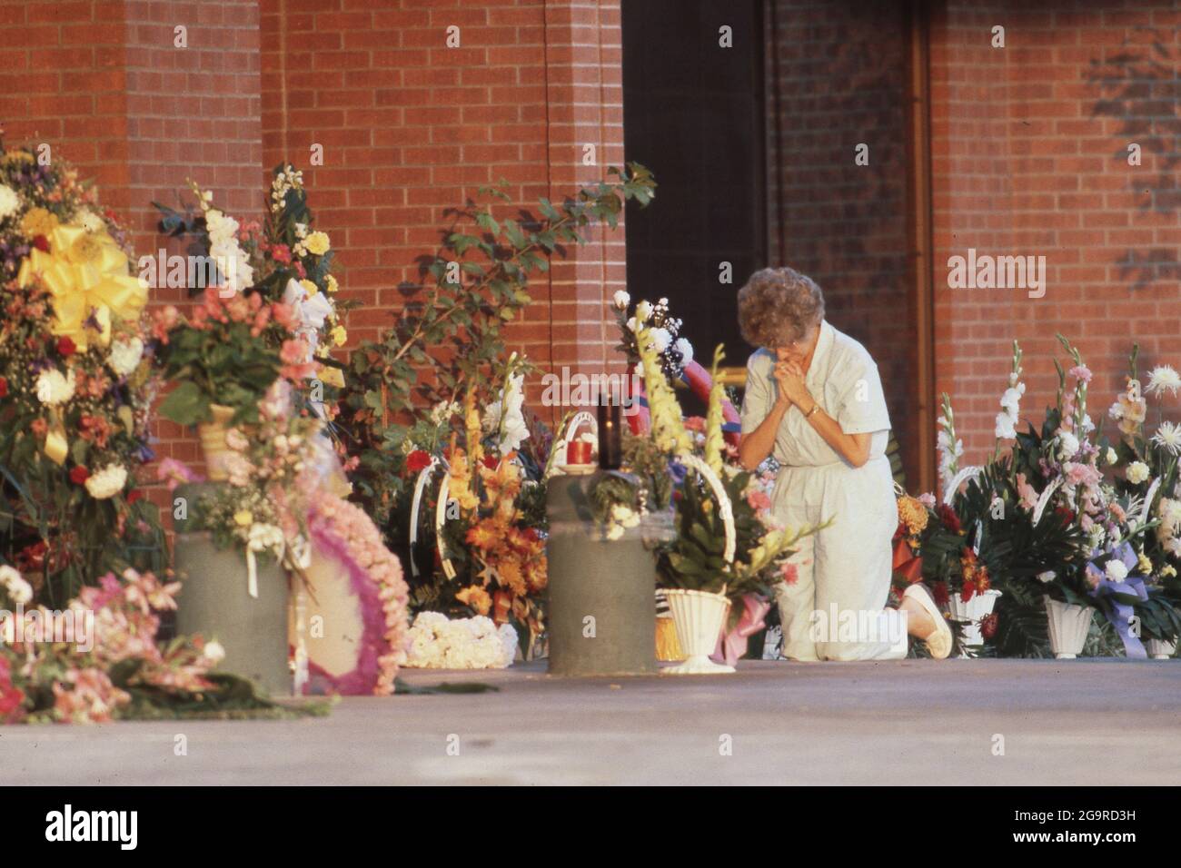 Killeen Texas USA, October 1991: Woman kneels in prayers among flowers left in memory of the victims of a mass shooting at Luby's Cafeteria in Killeen. on October 16. George Hennard, a 35-year-old Killeen resident, crashed a pickup into the eatery and shot 23 lunch-time diners and staff to death before killing himself. ©Bob Daemmrich Stock Photo