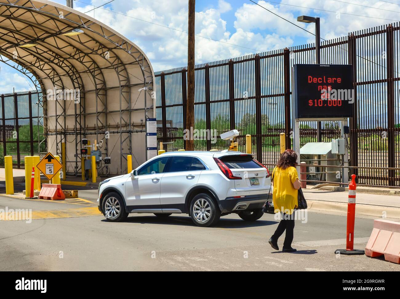 A woman in the crosswalk at the US-Mexican border with digital sign in Spanish annoucning the need to declare more than $10,000 upon entry, at border Stock Photo