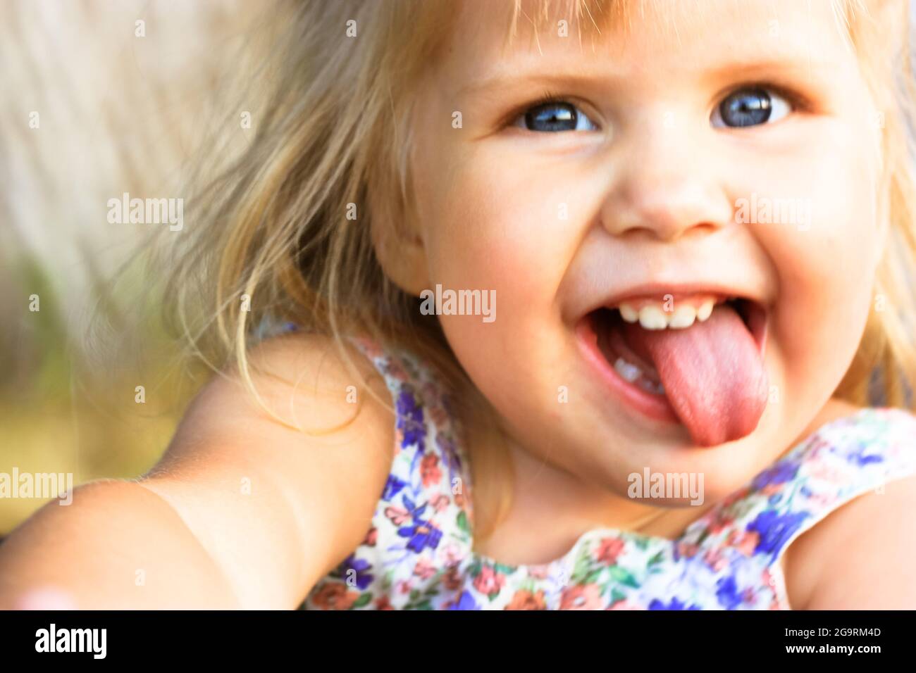 A funny infant 3 year happy old baby girl with open mouth and tongue out.  Emotional portrait of a playful cheerful blonde-haired, blue-eyed beautiful  Stock Photo - Alamy