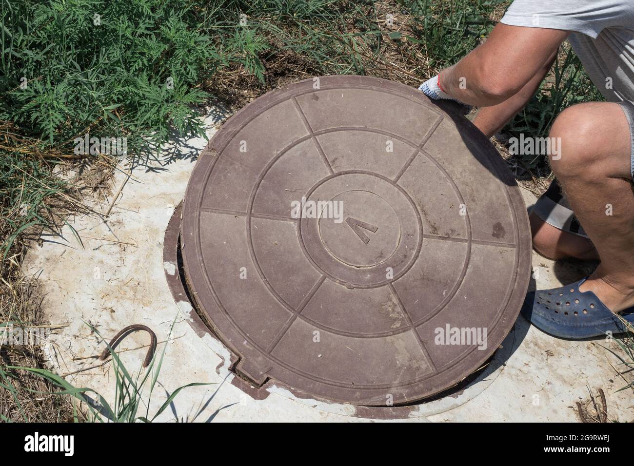 The man opens the manhole cover of the water well. Checking and fixing water metering. Stock Photo